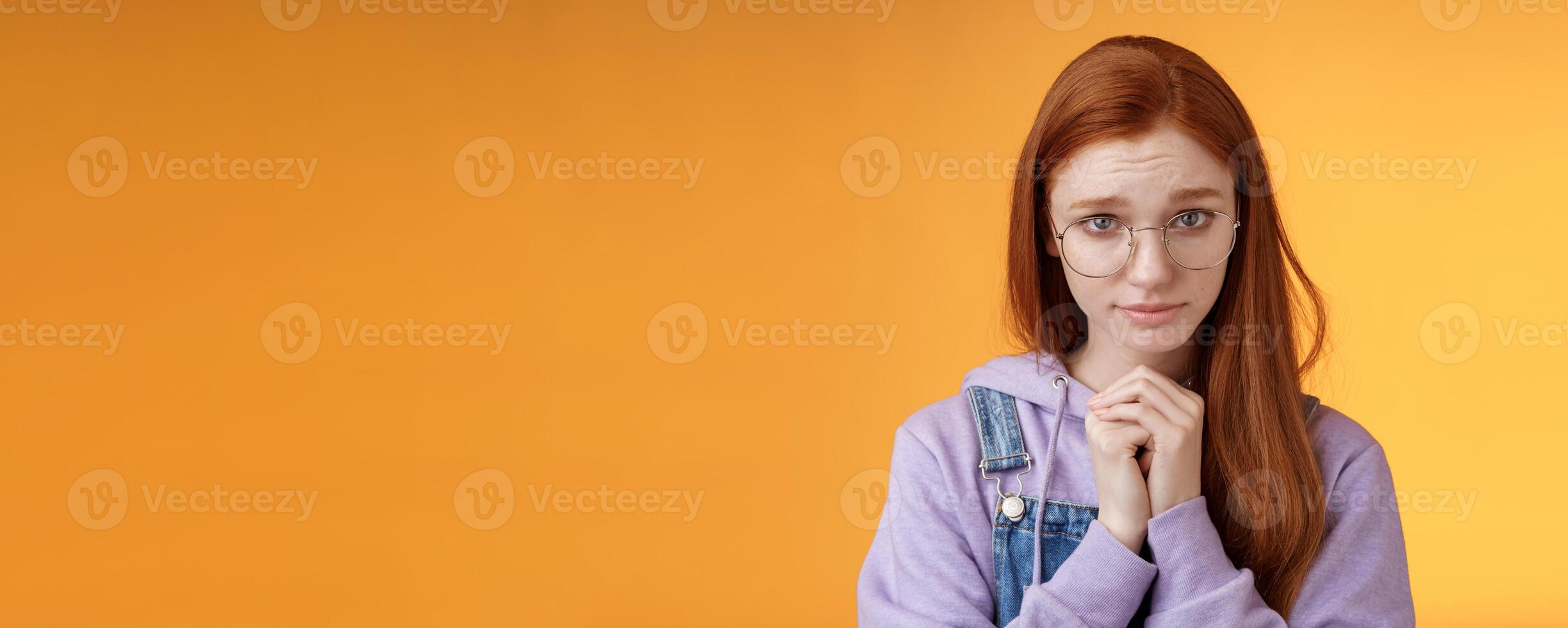 Silly guilty young shy redhead girlfriend asking forgiveness supplicating lower head look from under forehead frowning begging apology favour standing insecure sad pleading help, orange background photo