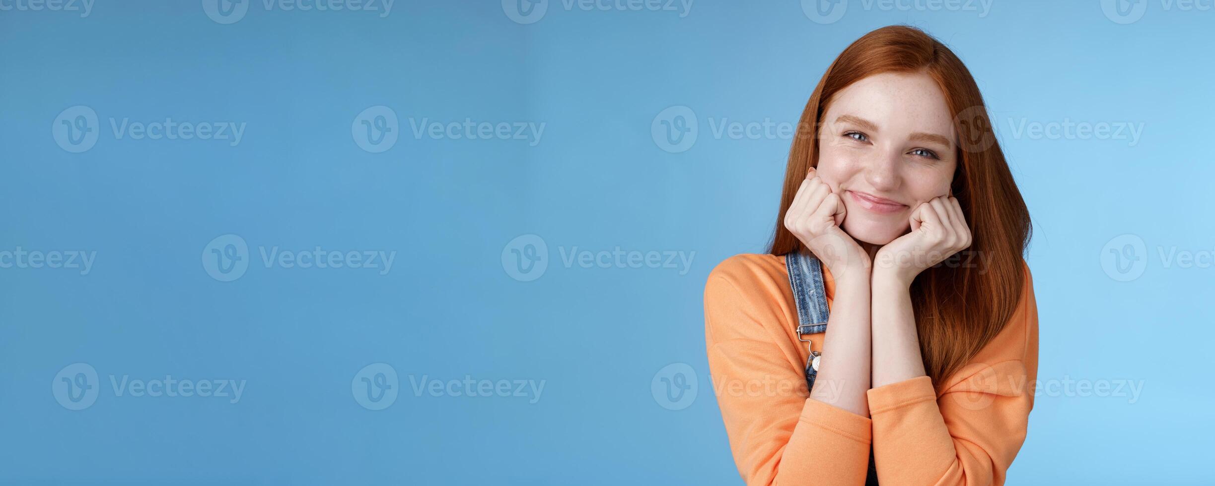 Tenderness, wellbeing, beauty conept. Attractive young ginger girl pure skin blue eyes lean palms silly smiling camera look amused enthusiastic listen interesting stories gladly, blue background photo