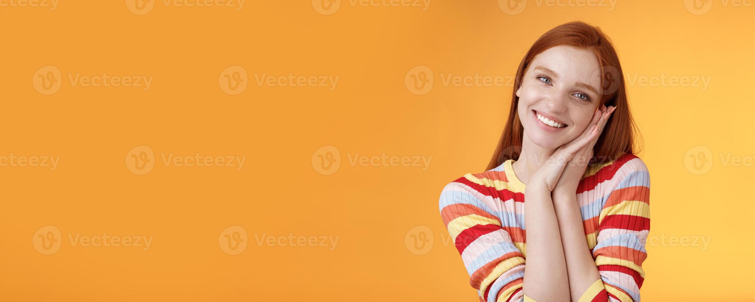 Lovely young flirty redhead european girl smiling broadly excited happy lean palm receive sweet tender present look grateful amused joyfully reacting pleasing moment, standing orange background photo