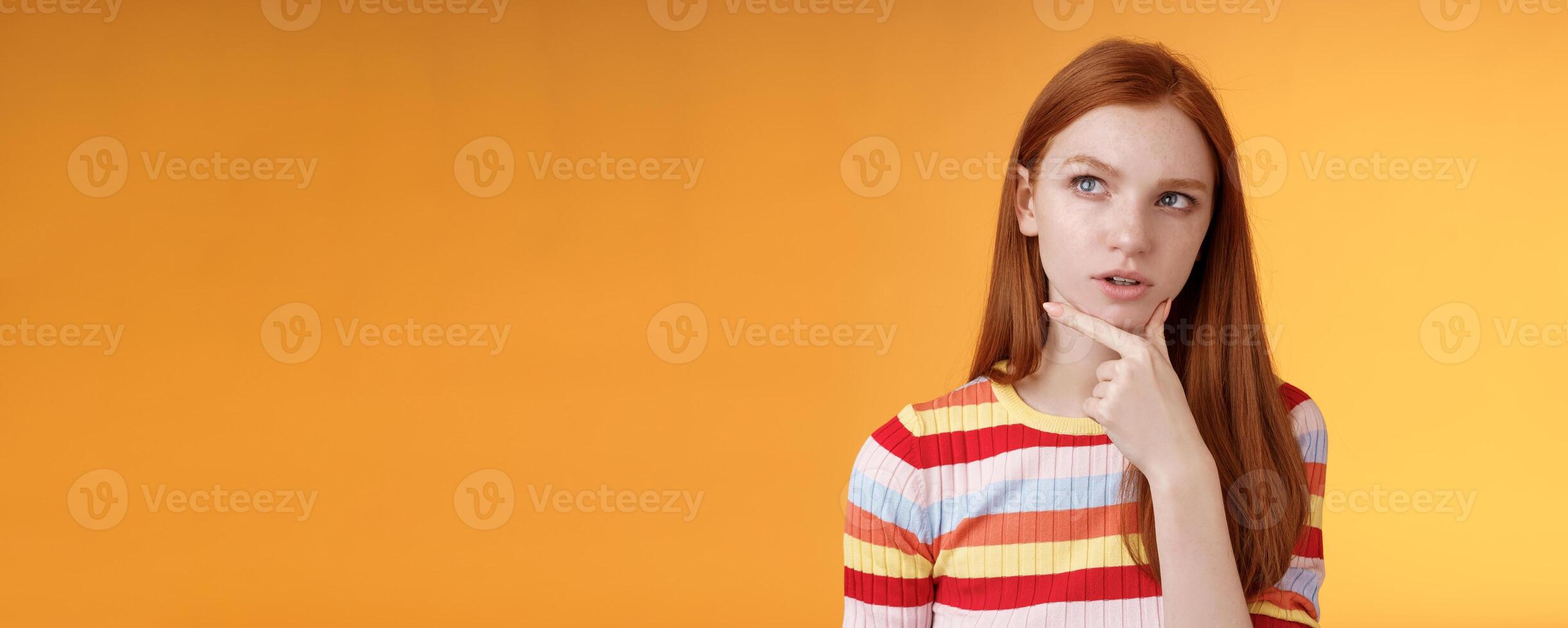Smart creative serious-looking redhead female coworker thinking deep focus pondering idea making choice touching chin thoughtful look upper left corner questioned puzzled orange background photo
