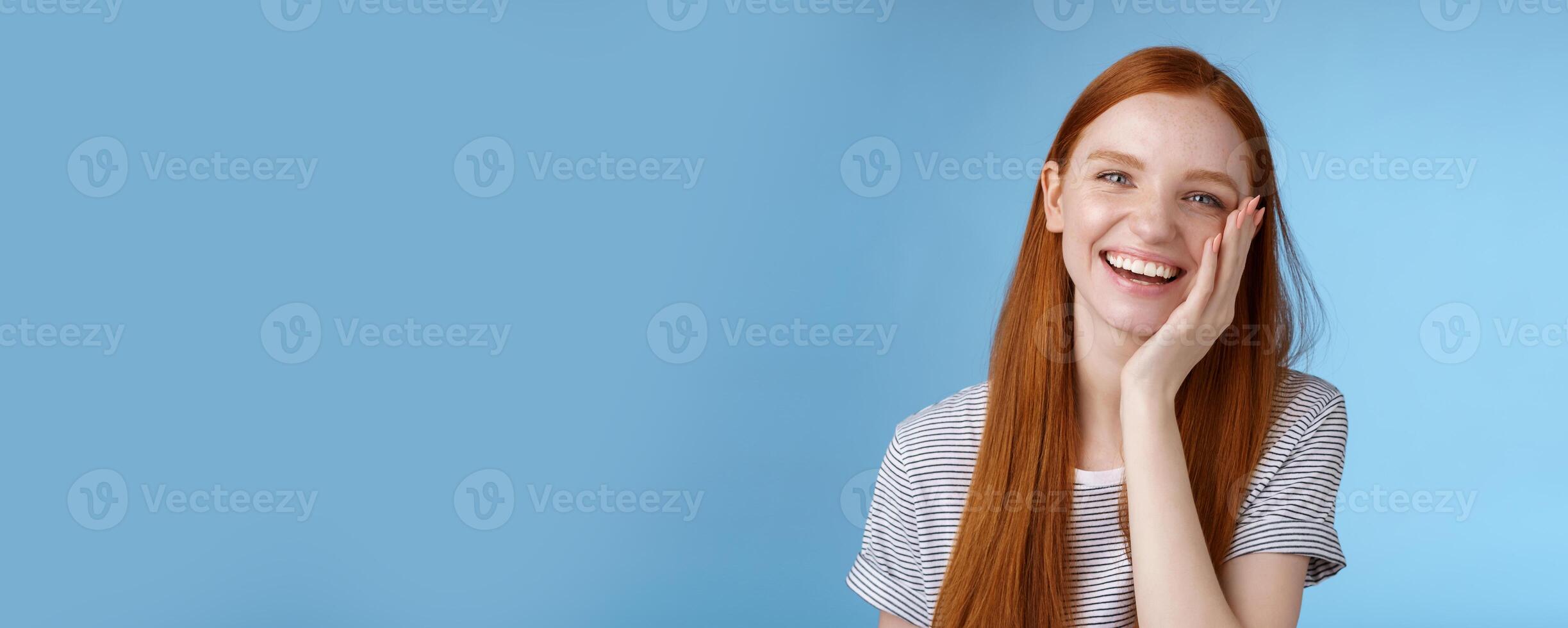 Charismatic talkative friendly-looking happy laughing redhead girl having fun discuss previous summer holidays make jokes chuckling touching face amused standing cheerful blue background photo