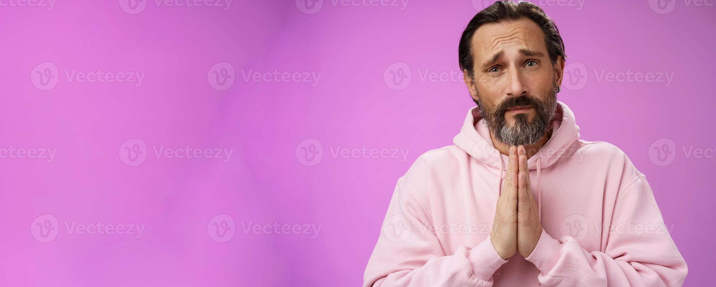 Upset handsome bearded mature man need help asking forgiveness supplicating press palms together praying frowning sorrow begging favour lend money, standing purple background miserable photo