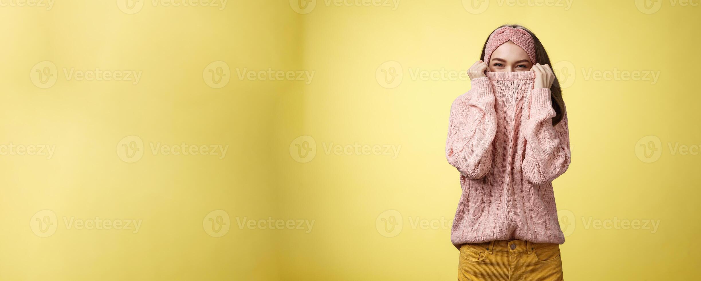 Cute playful young girl hiding in sweater peeking and squinting flirty over top of cloth pulling collar on nose, fooling around having fun happily, being in positive good mood, warming-up on cold day photo