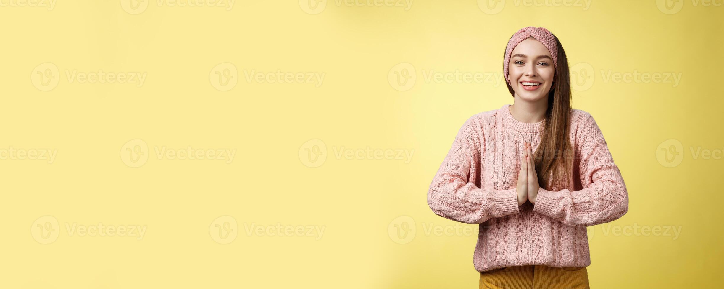 Please do me favour. Charming young female student wearing knitted sweater, headband pressing palms together in pray begging, asking for help smiling thankful, grateful for effort over yellow wall photo