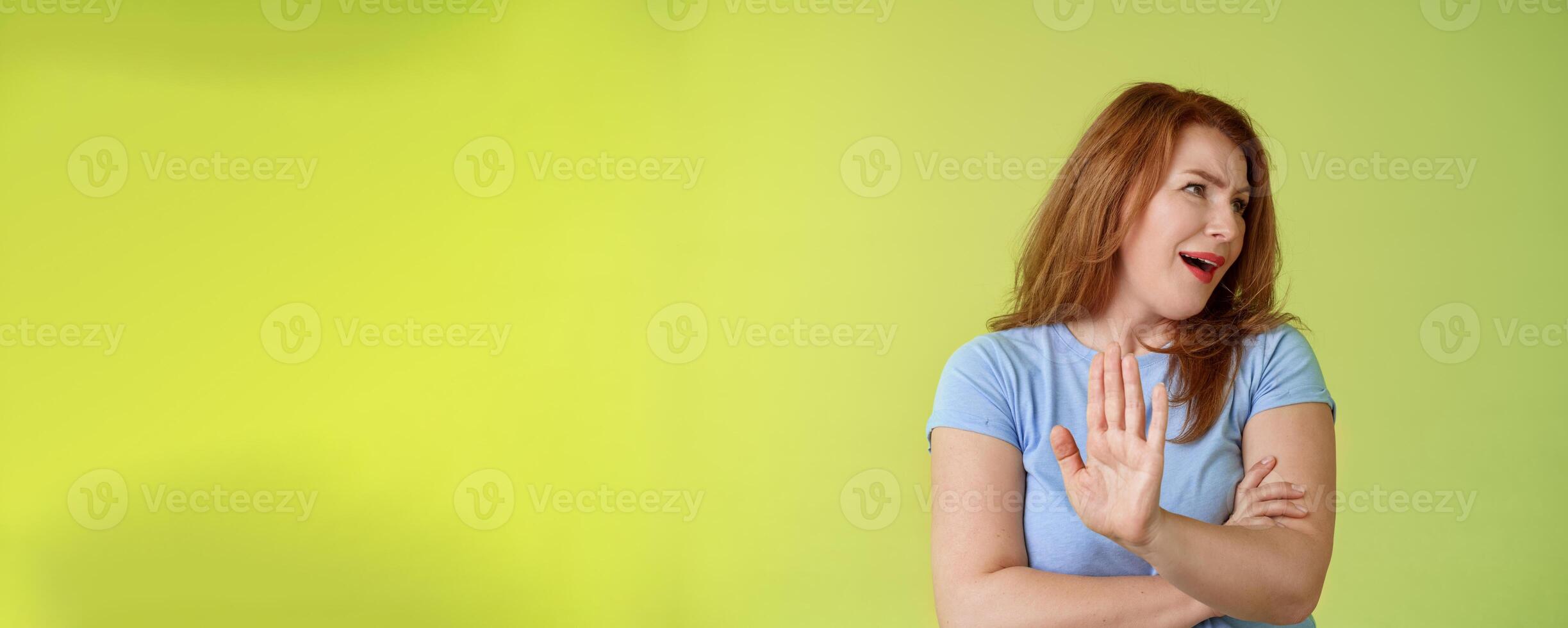 Enough wasting my time. Ignorant uninterested redhead mature woman turn away displeased reluctant show stop no gesture hold palm refusal rejecting unpleasant offer green background photo