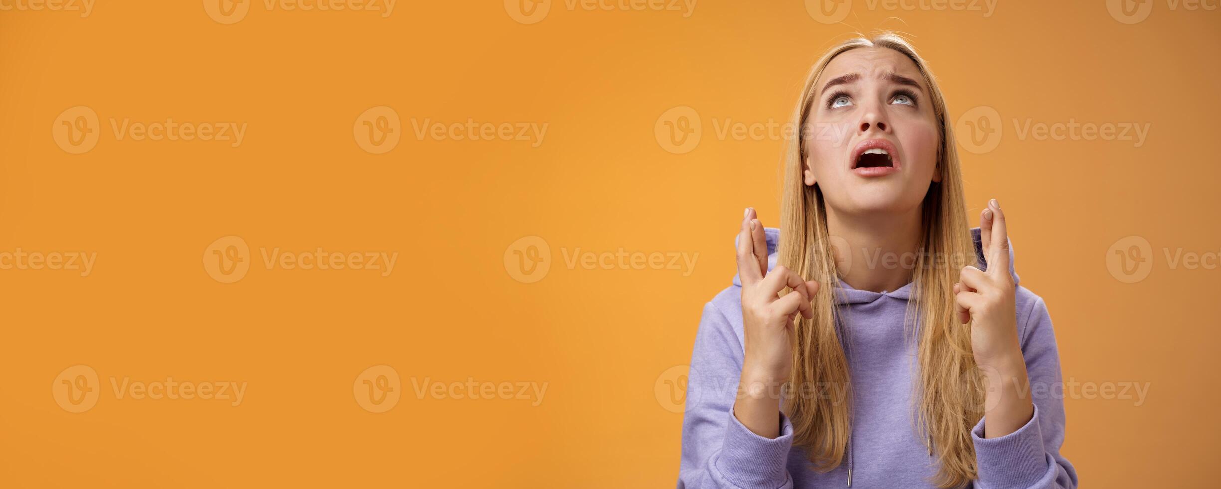 Worried nervous cute blond woman in hoodie begging god help cross fingers good luck supplicating look up skies wanna win anticipating good news anxiously awaiting, orange background photo