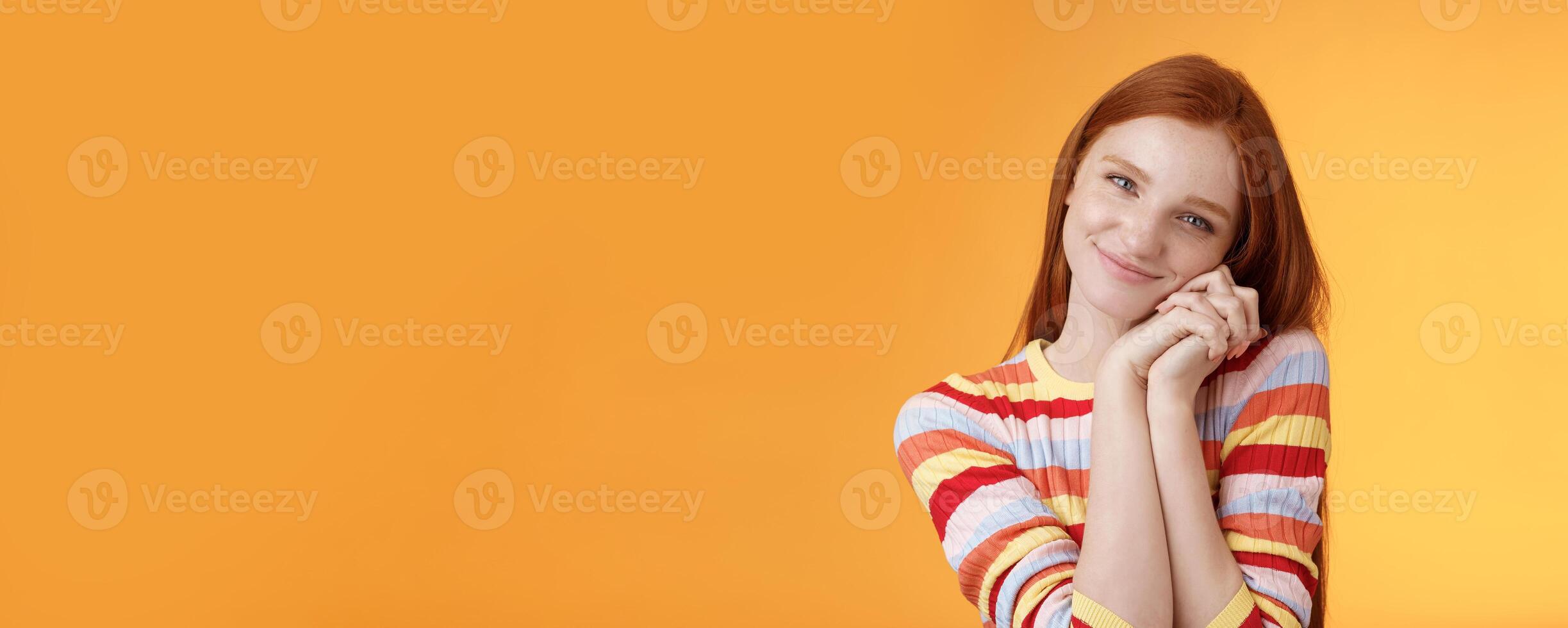 Sweet silly tender redhead young girl leaning palms touched smiling receive charming lovely gift standing thankful look affection sympathy accept dearest romantic gesture, orange background photo