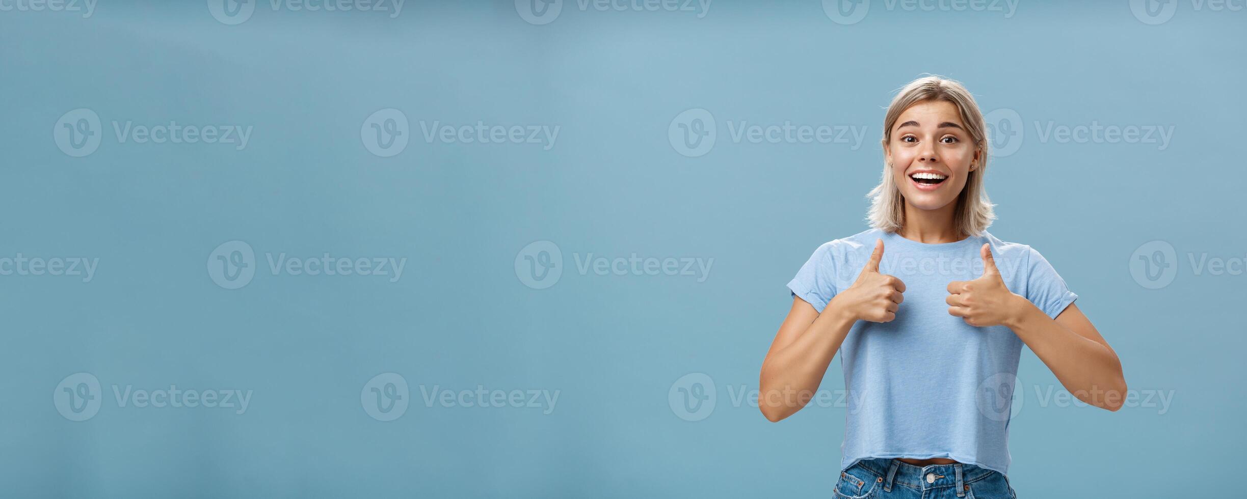 You did great proud of you. Portrait of satisfied and fascinated attractive happy girlfriend in casual t-shirt showing thumbs up and smiling broadly being supportive and cheerful over blue wall photo
