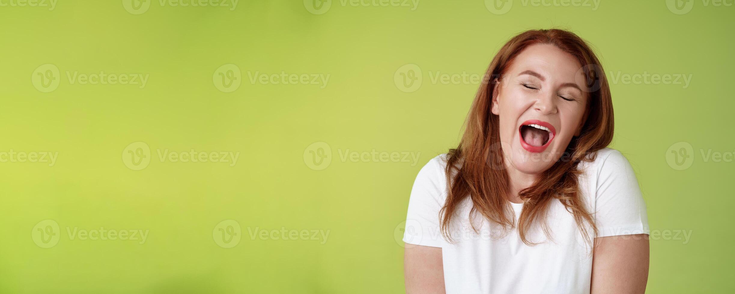 Lazy weekends finally time sleep. Cheerful redhead middle-aged 50s woman yawning satisfied close eyes feel sleepy wake up early morning wanna take nap stand green background watching boring film photo