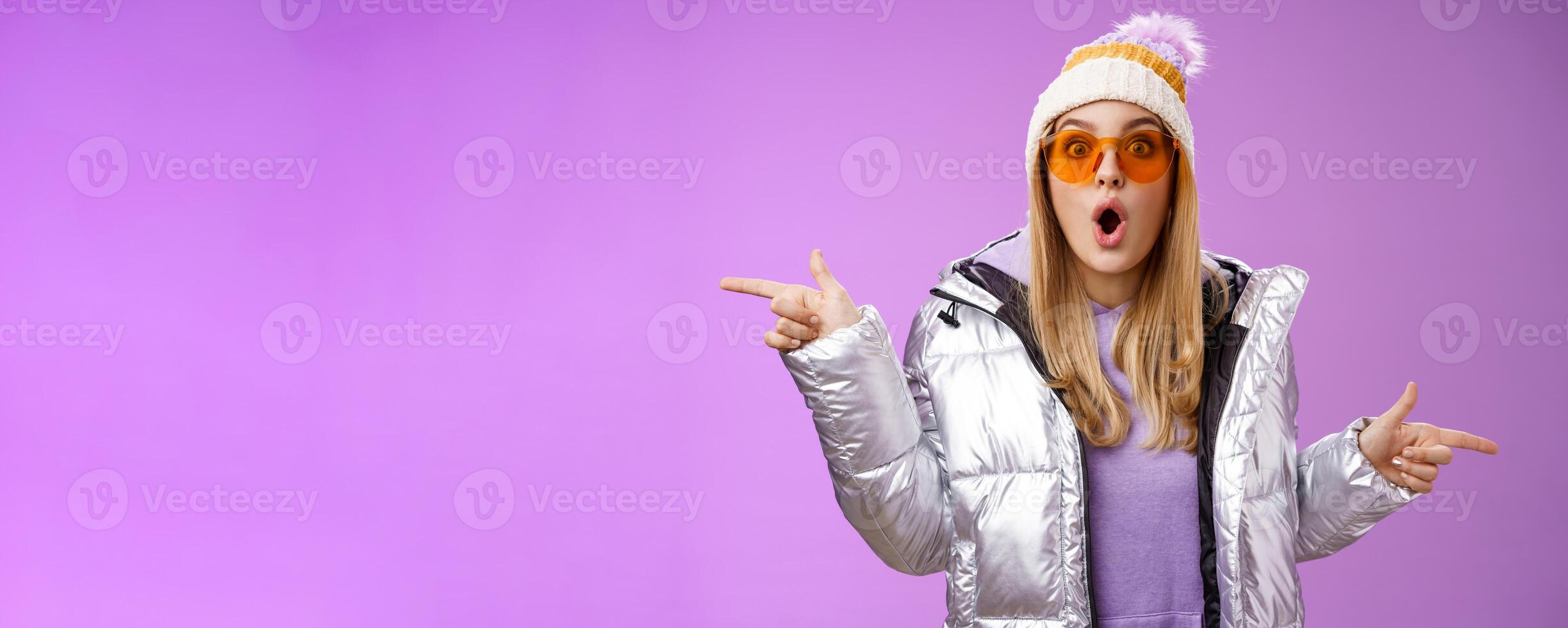 Impressed blond girl gasping widen eyes surprised folding lips wow sound check out incredible discounts winter equipment pointing left right cannot choose standing astonished purple background photo