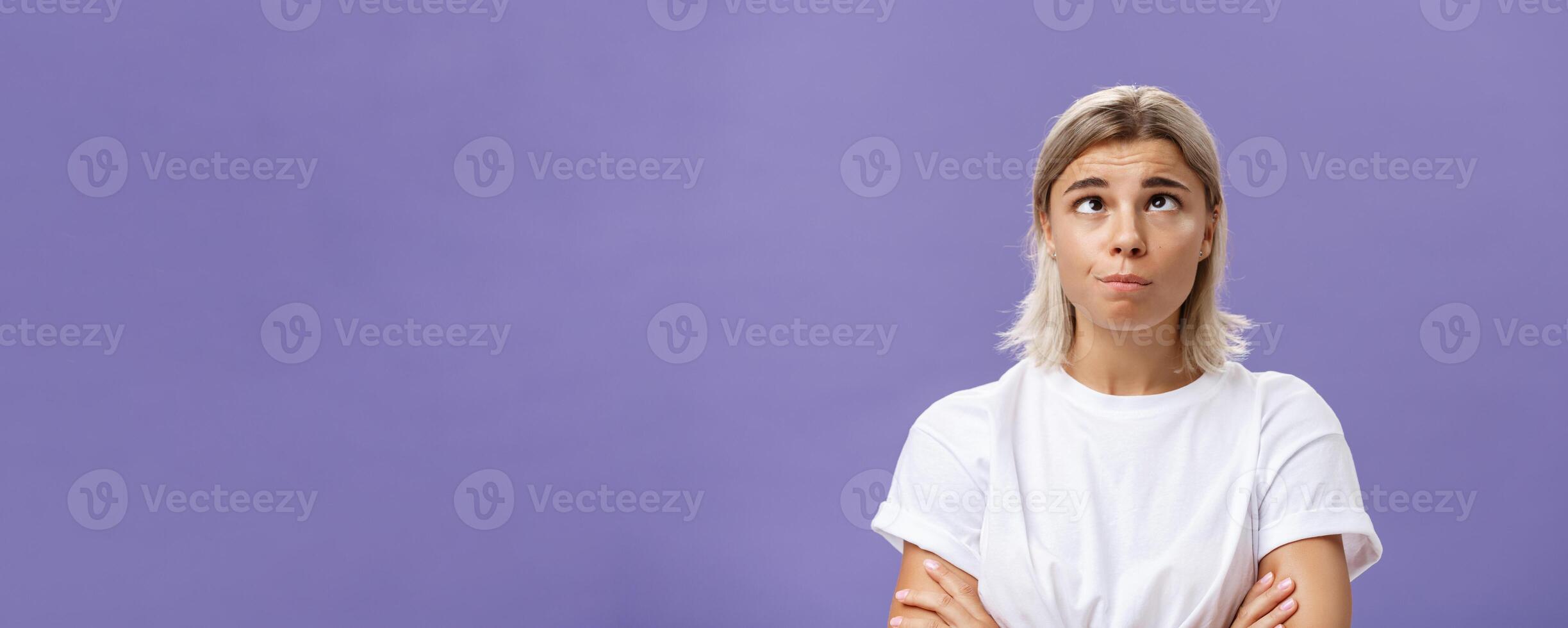 Mind going crazy. Portrait of funny tired attractive young woman with fair hair and tanned skin squinting rolling eyes aside and looking up fooling around over purple background from boredom photo