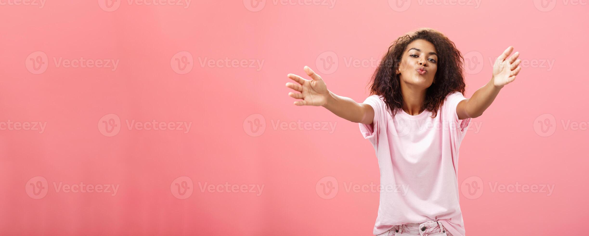 Come closer let me hug you. Portrait of passionate confident and happy good-looking african american woman with curly hairstyle folding lips pulling hands towards camera to cuddle and give kiss photo