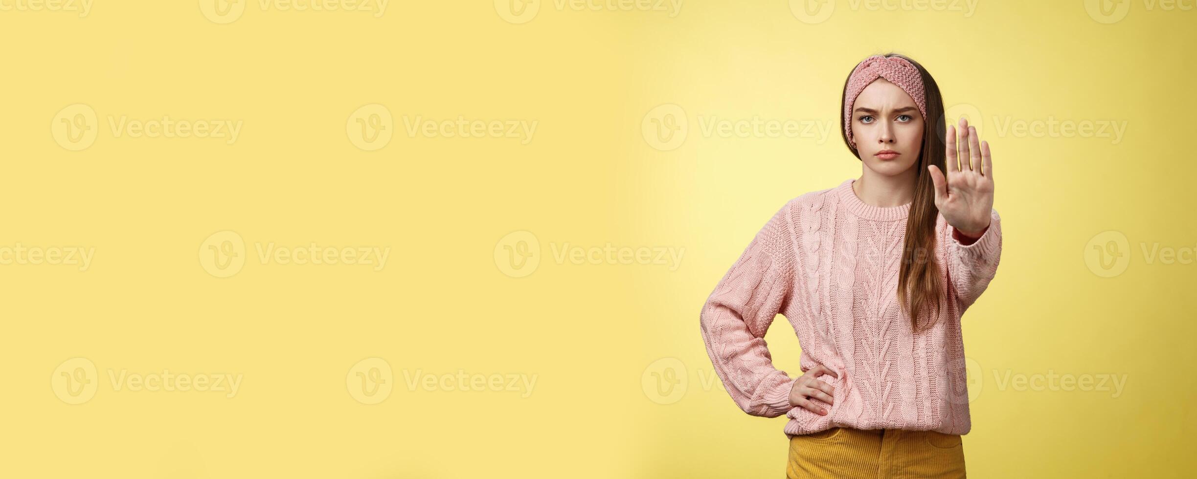 Stop it. Serious-looking confident focused young cute girl extending arm hold, tresspass gesture, frowning displeased, standing bossy denying, forbidding pass, unwilling let-through over yellow wall photo