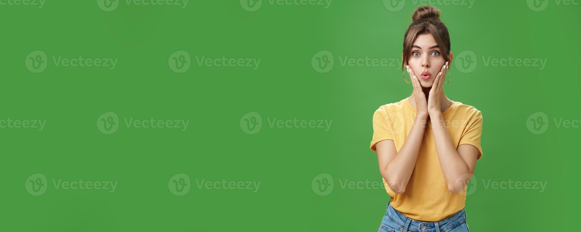 Silly cute and tender young female model with cleacn skin folding lips, pressing hands to cheeks and looking at camera taking care of acne and imperfactions using daily skincare products photo