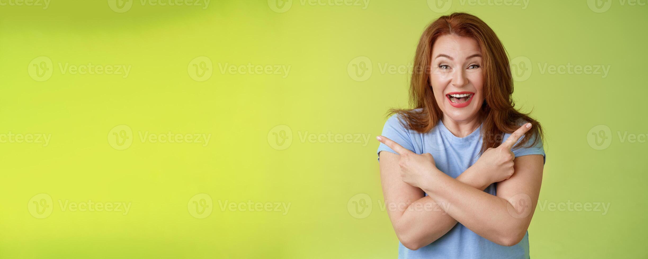 Happy carefree entushiastic redhead funny mature female having fun positive attitude cross arms body pointing sideways show left right products laughing happily like both choices green background photo