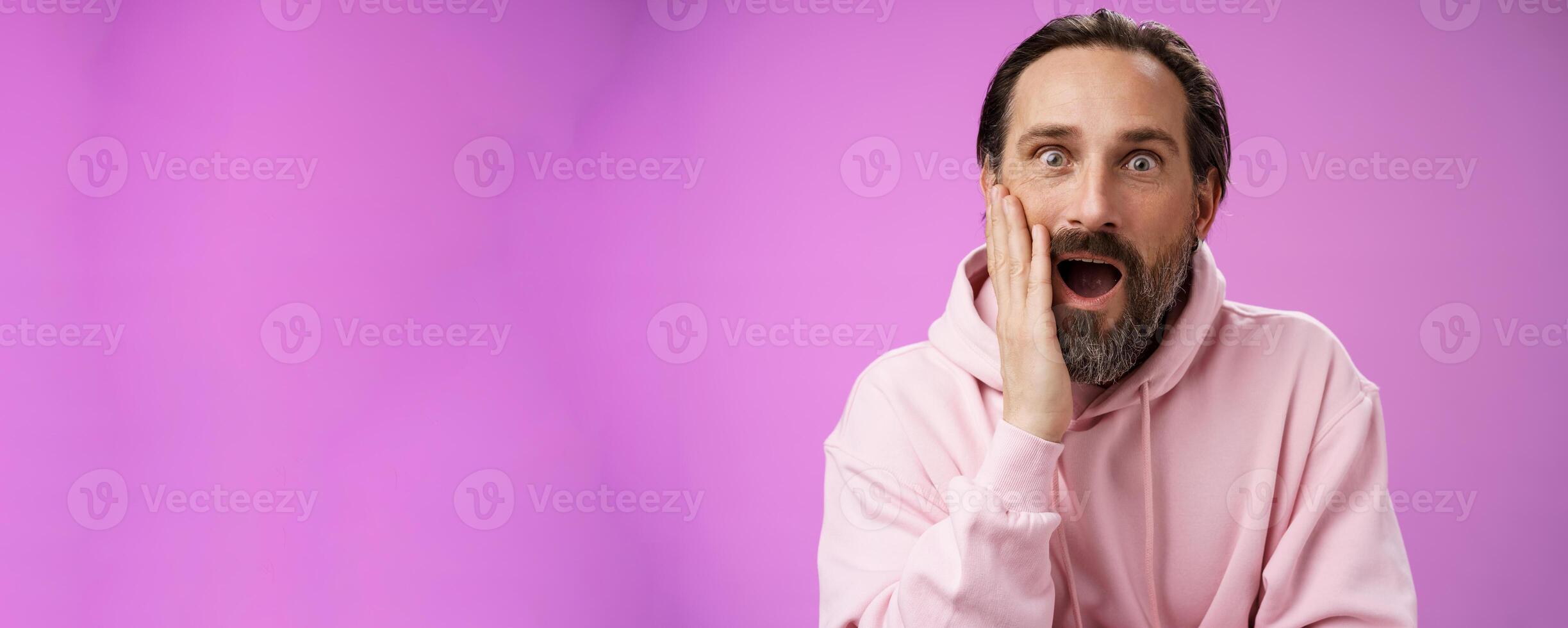 Impressed fascinated speechless mature male attend interesting lecture drop jaw thrilled touch cheek palm widen eyes surpised astonished, standing purple background amzed and amused photo