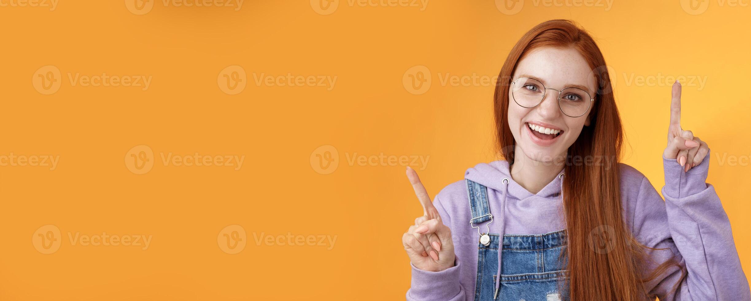 Lively enthusiastic millennial redhead girl coworker having fun celebrating small break joyfully dancing pointing up index fingers singing smiling white teeth promoting product, orange background photo