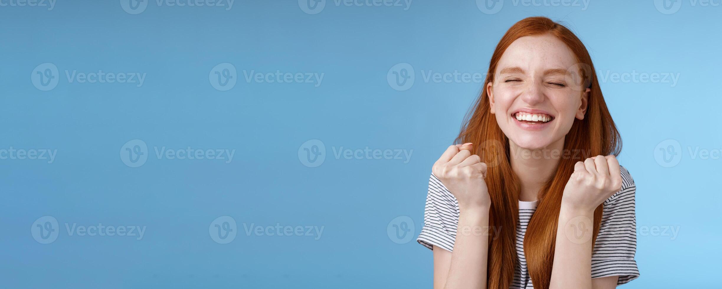 Happy accomplished good-looking ginger girl receive positive results test clench fists rejoicing yelling yes celebrating do winner dance close eyes relieved standing blue background triumphing photo