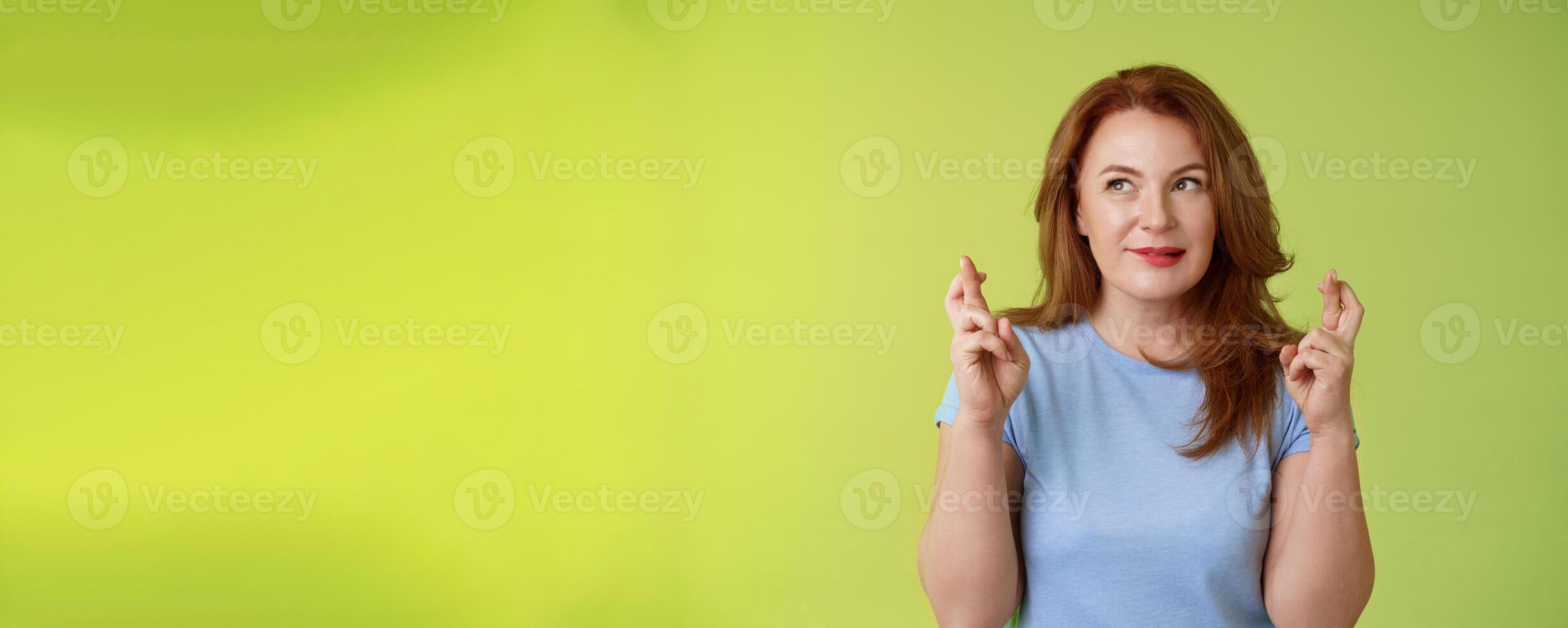 Hopeful enthusiastic ginger middle-aged redhead female praying believe dream come true awaiting miracle anticipating good positive results bite lip temptation look aside make wish cross fingers luck photo