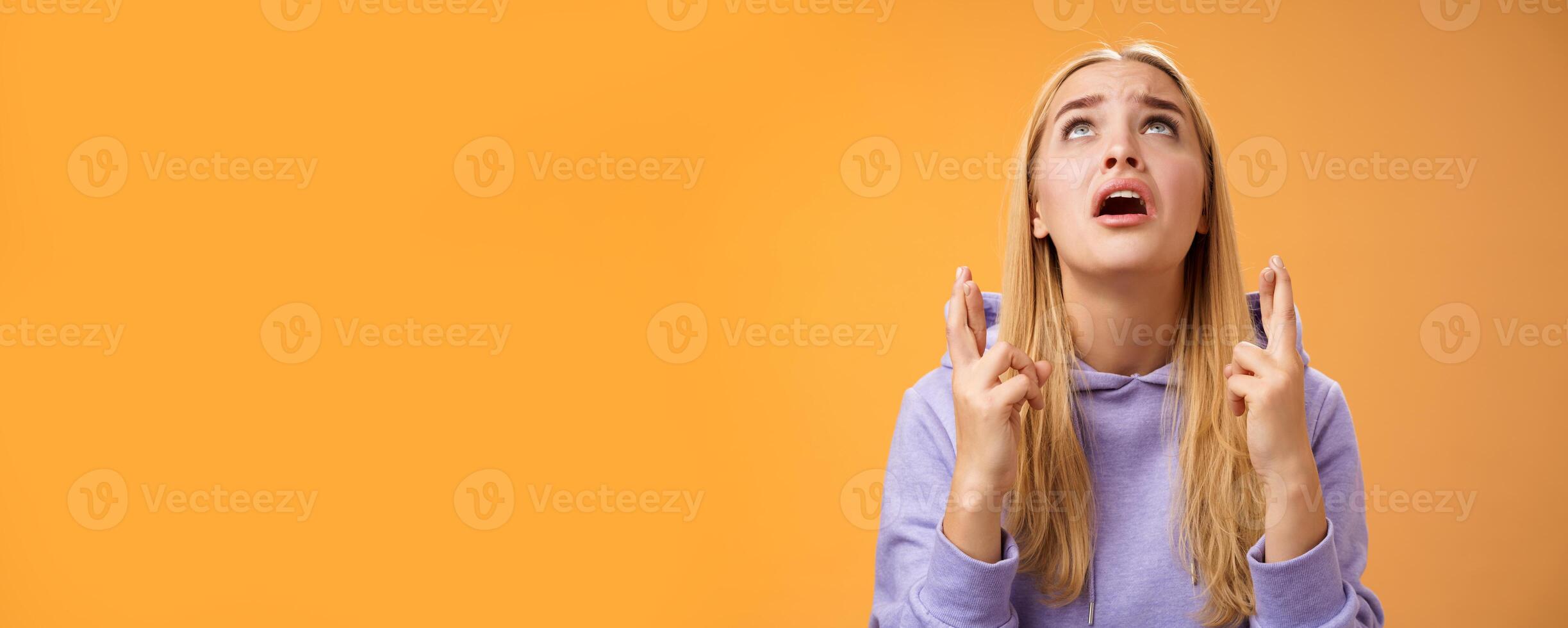 Worried nervous cute blond woman in hoodie begging god help cross fingers good luck supplicating look up skies wanna win anticipating good news anxiously awaiting, orange background photo