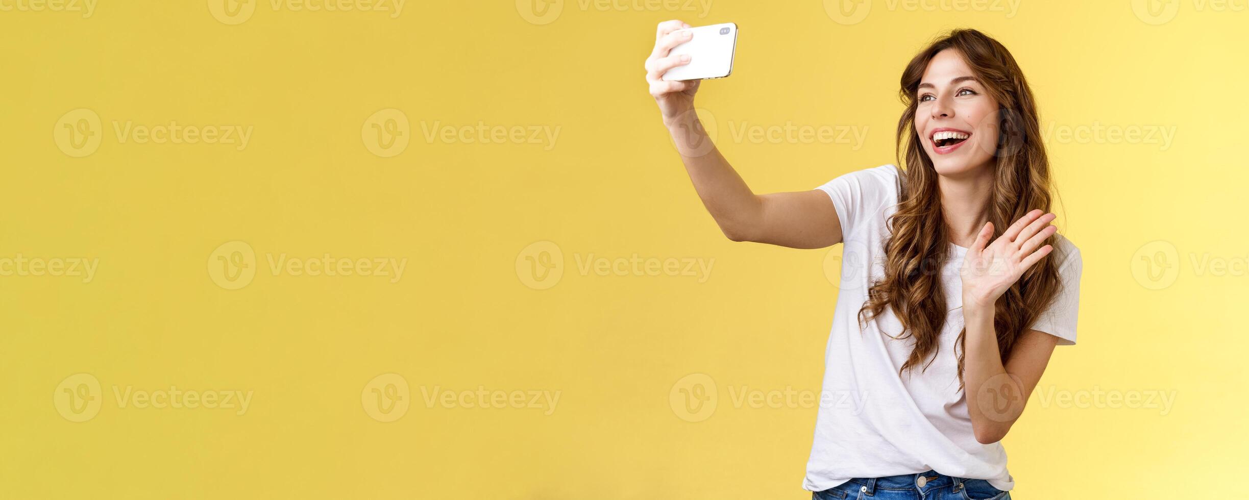 Friendly lively good-looking cheerful feminine girl extend arm hold smartphone record blog waving front camera smiling broadly talking fans videocalling taking selfie yellow background photo