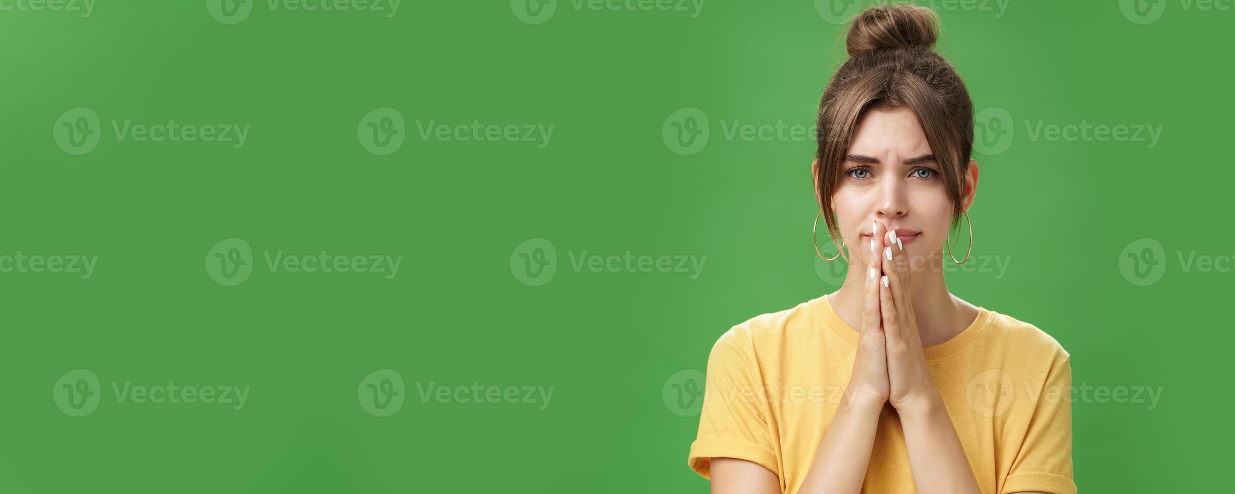 Waist-up shot of nervous upset girlfriend holding hands in pray over lips frowning looking concerned worrying for boyfriend standing anxious and sad over green background photo