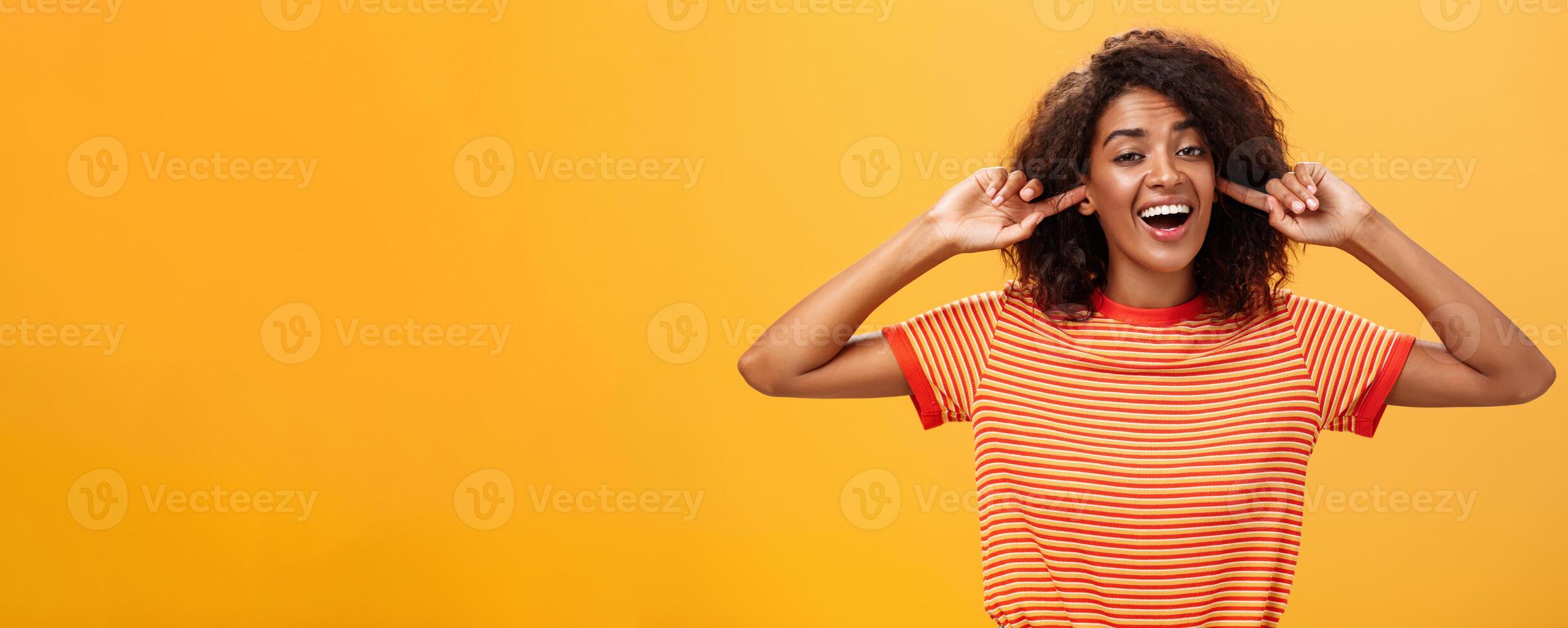 Do not care what saying cannot hear you. Carefree indifferent good-looking african american woman with curly hairstyle closing ears with index finger singing lalala during argument behaving childish photo