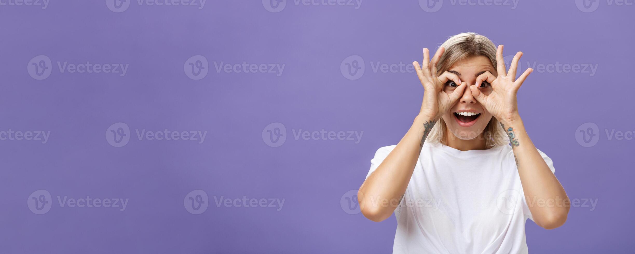 Looking at awesome discounts. Portrait of impressed amused and happy good-looking stylish young woman with tattoos on arms making circles with hands over eyes smiling with admiration at camera photo