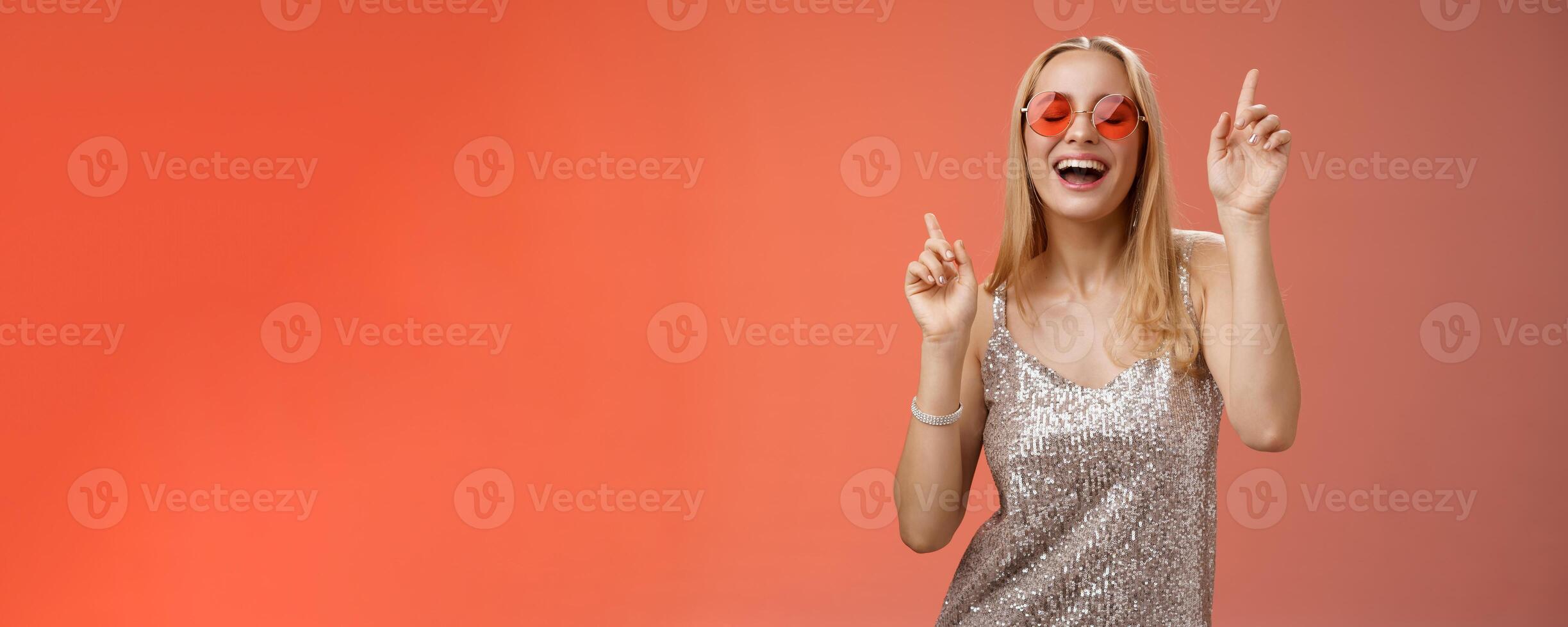Amused attractive happy smiling woman dancing nightclub having fun enjoying go wild party celebrating b-day wearing stylish dress sunglasses raise index fingers smiling singing along photo