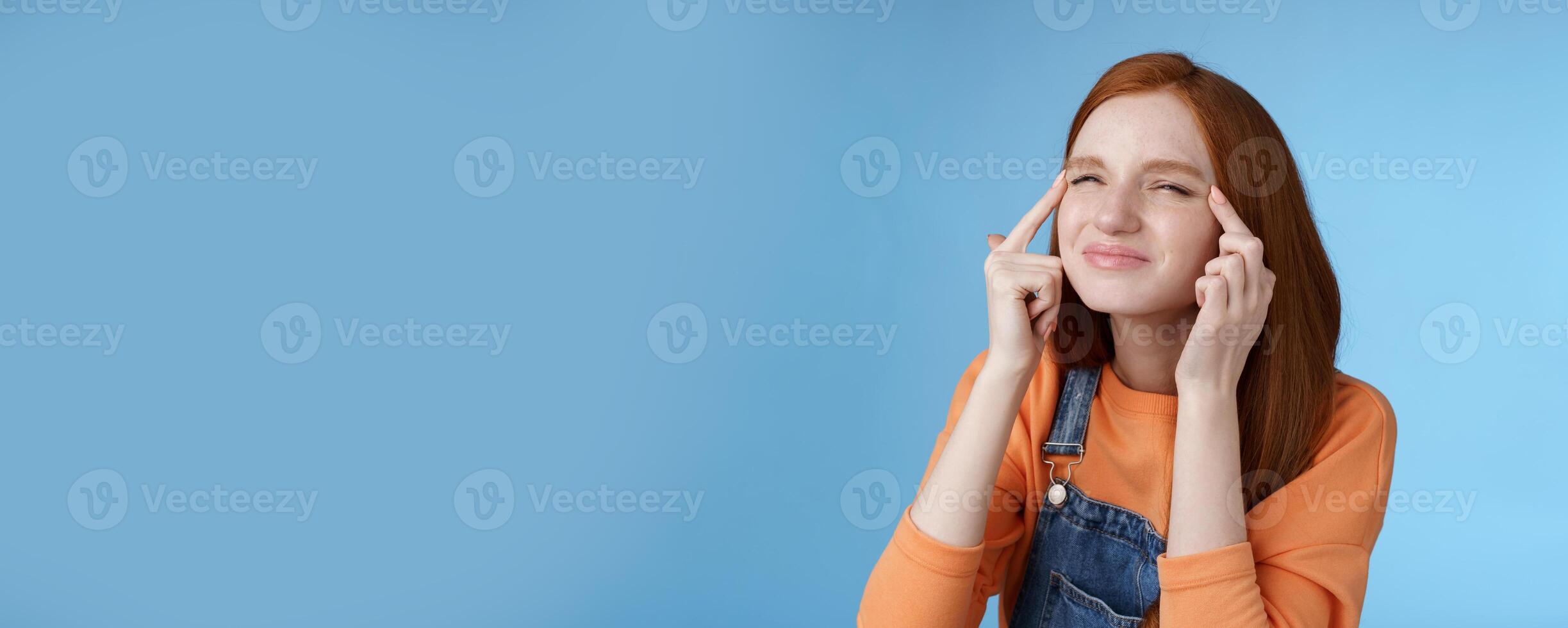 Cute funny european redhead girl forgot glasses trying read sigh stretch eyelids squinting frowning focused look upper left corner perplexed see what happening, standing blue background photo