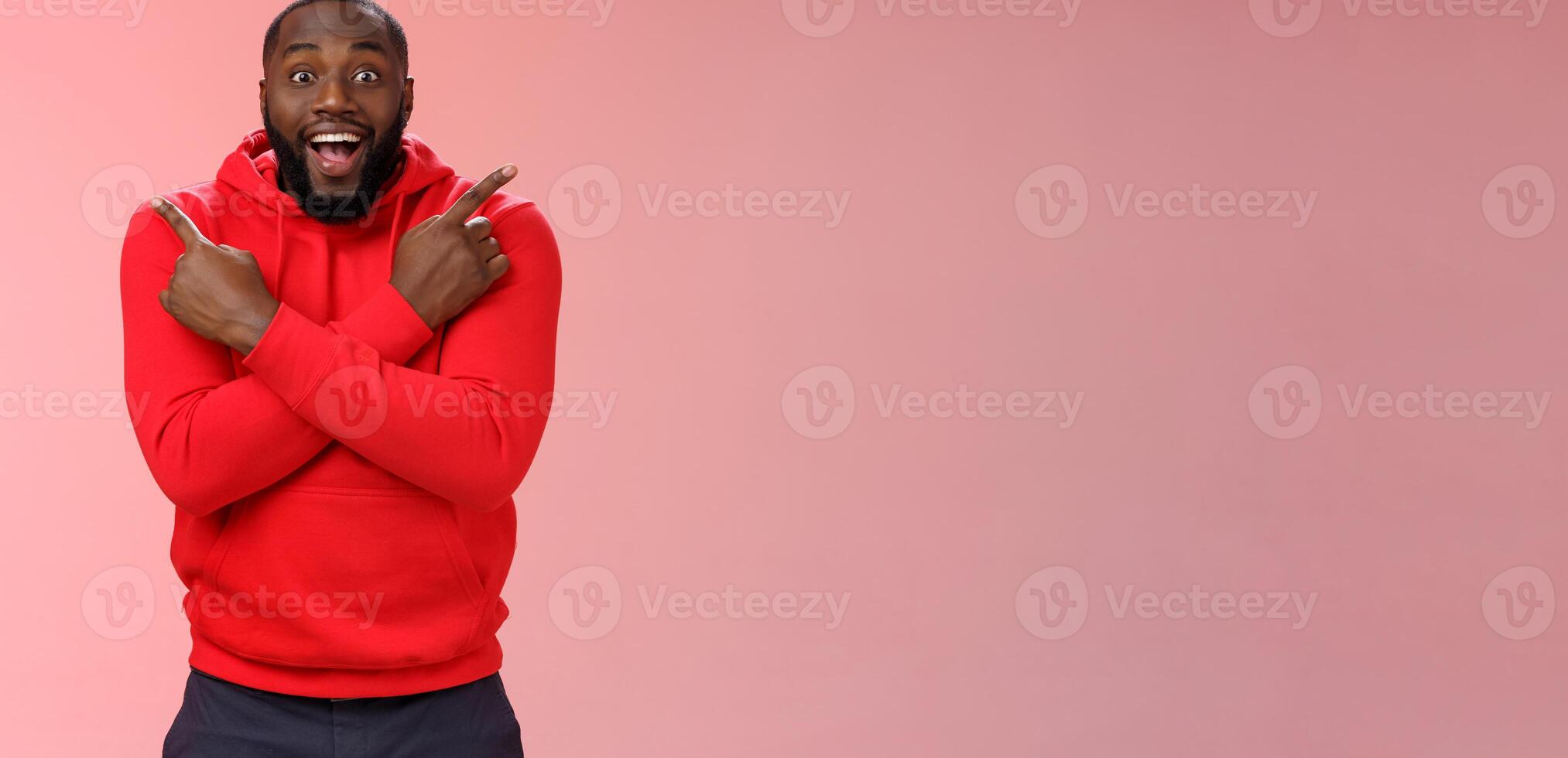 Glad amazed good-looking happy black male customer bearded widen eyes surprised joyfully pointing both sides left right cross arms chest impressed variety cool products, standing pink background photo