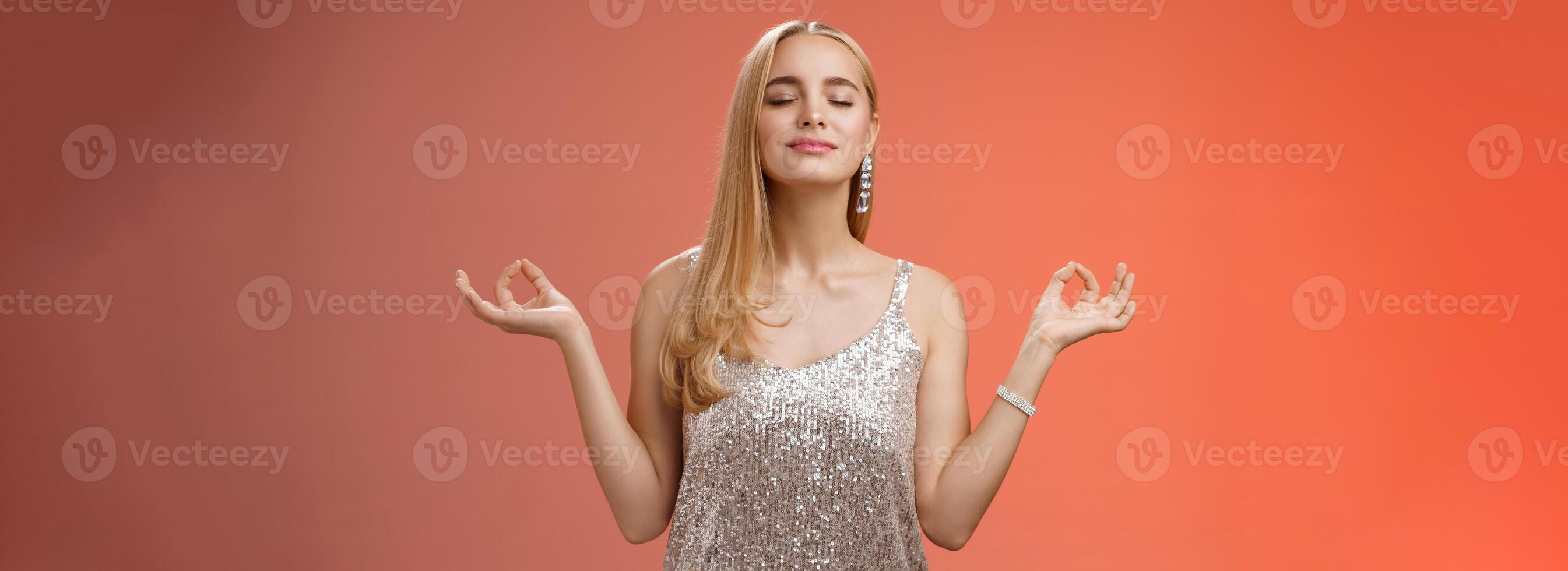 Keep calm party all night. Carefree unbothered happy charming stress-free blond young woman in stylish dress smiling relieved close eyes rejoicing standing lotus nirvana pose, breathing meditating photo