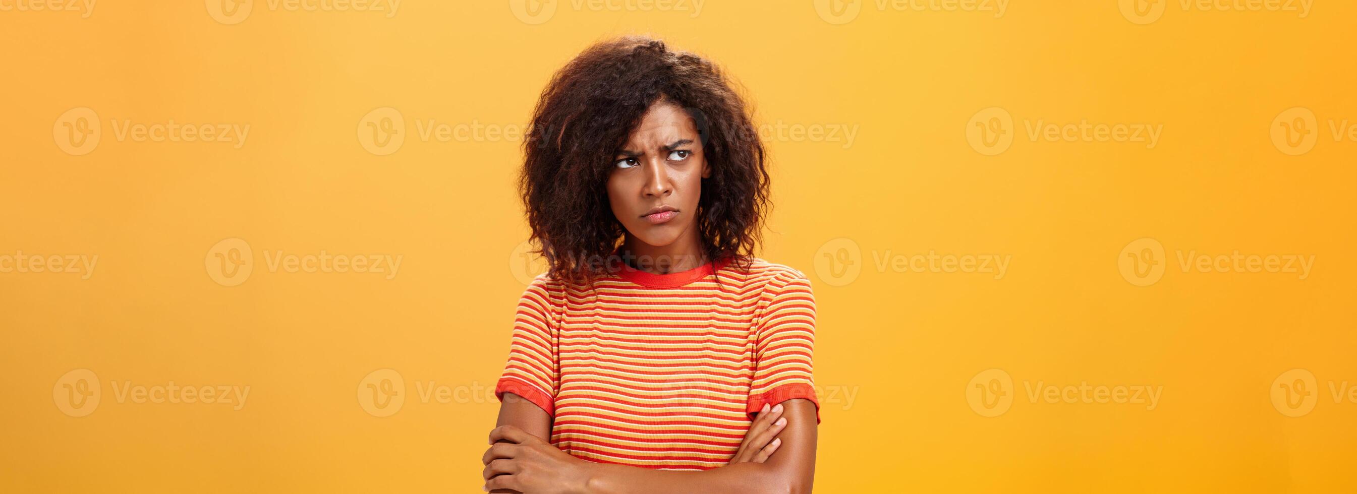 Why life so cruel and unfair. Gloomy displeased and sad cute african american young woman with curly hairstyle crossing arms on chest in offended pose frowning looking left jealous and unhappy photo