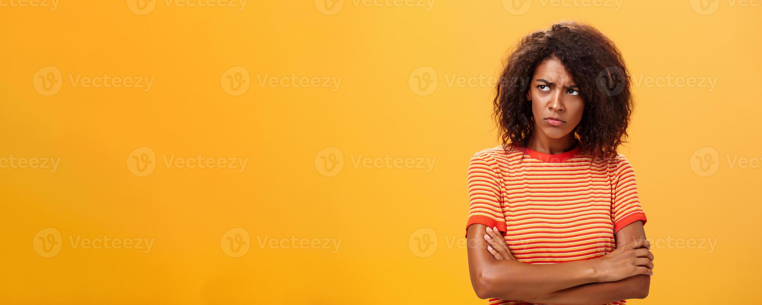 Why life so cruel and unfair. Gloomy displeased and sad cute african american young woman with curly hairstyle crossing arms on chest in offended pose frowning looking left jealous and unhappy photo