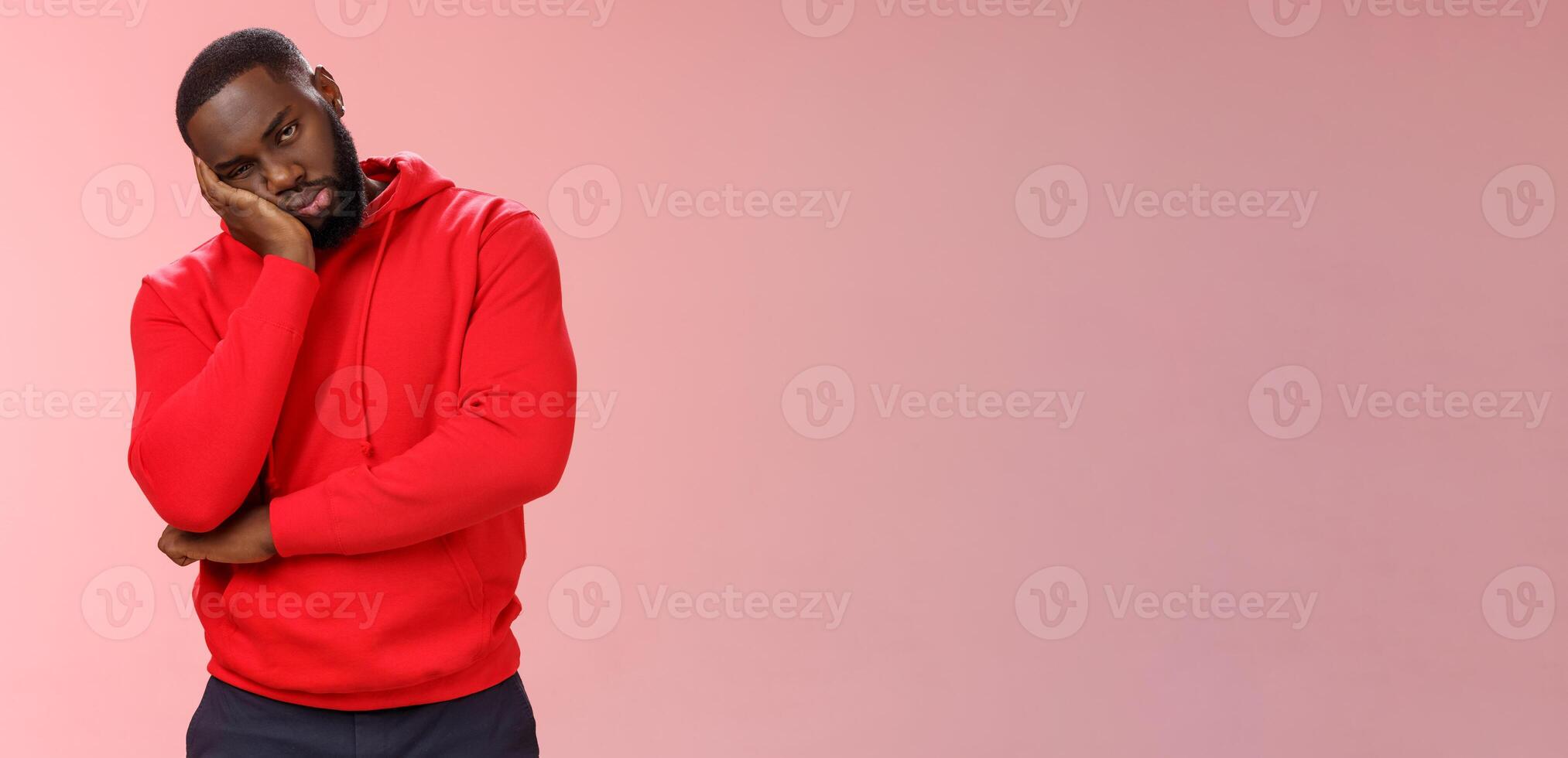 Bored young 25s black guy in red hoodie facepalm lean head hand look indifferent sleepy attend boring meeting fall asleep carelessly listening uninteresting story, pink background photo