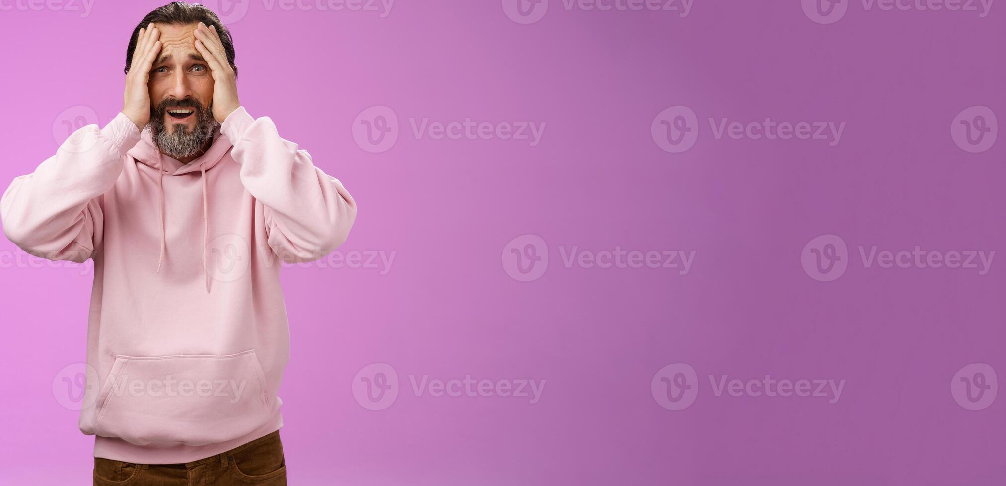 Adult upset bearded man despair standing troubled concerned touching face frowning grimacing sorrow unhappiness, losing bet, was robbed, standing shocked devastated purple background, panic photo
