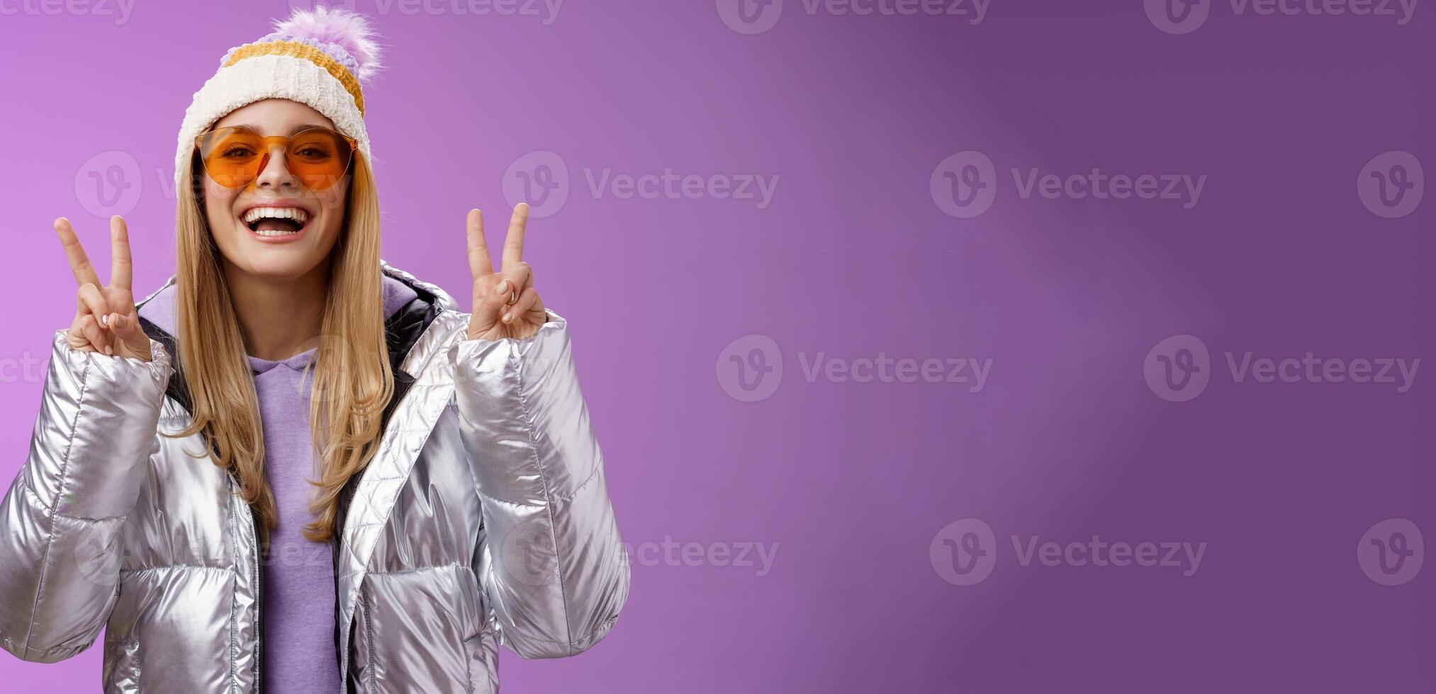 Friendly lucky optimistic beautiful blond woman in sunglasses silver stylish jacket winter hat show peace victory gesture enjoying snowy vacation get outside hotel enjoy skiing, purple background photo