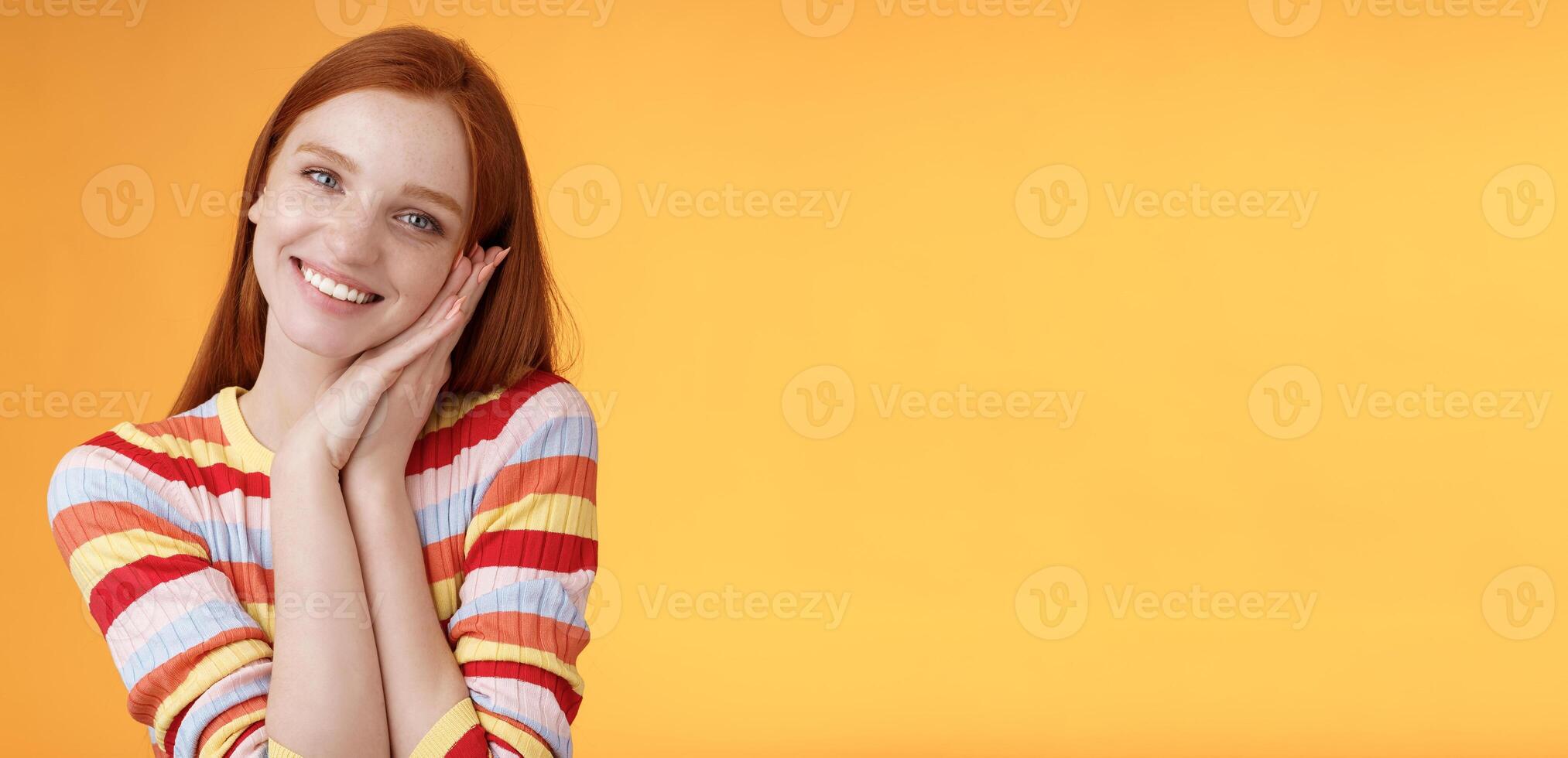 Lovely young flirty redhead european girl smiling broadly excited happy lean palm receive sweet tender present look grateful amused joyfully reacting pleasing moment, standing orange background photo