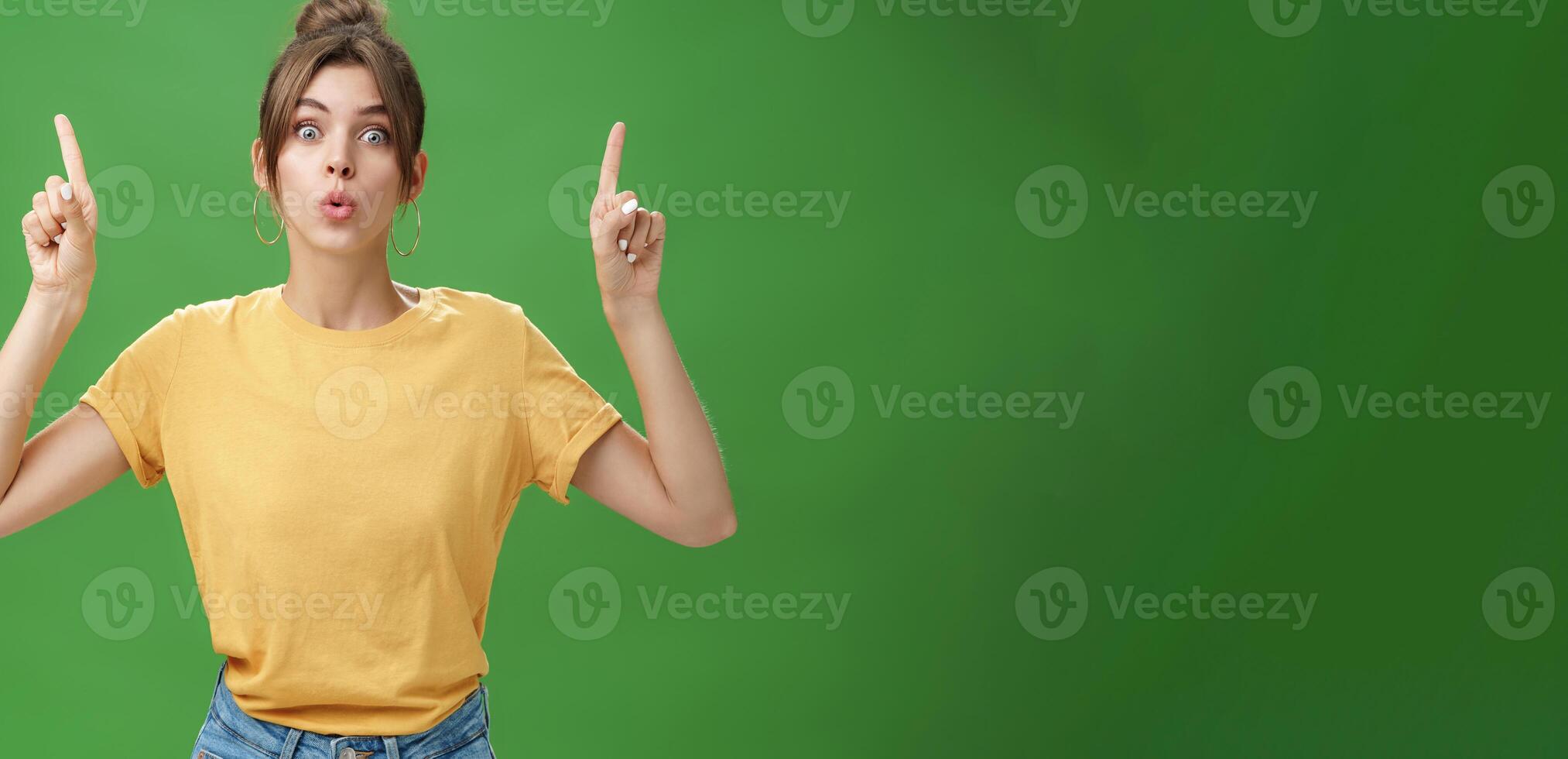 Authentic good-looking woman with natural beauty and tattoo on arm raising index fingers pointing up folding lips from interest and curiosity reacting impressed and excited at awesome advertisement photo