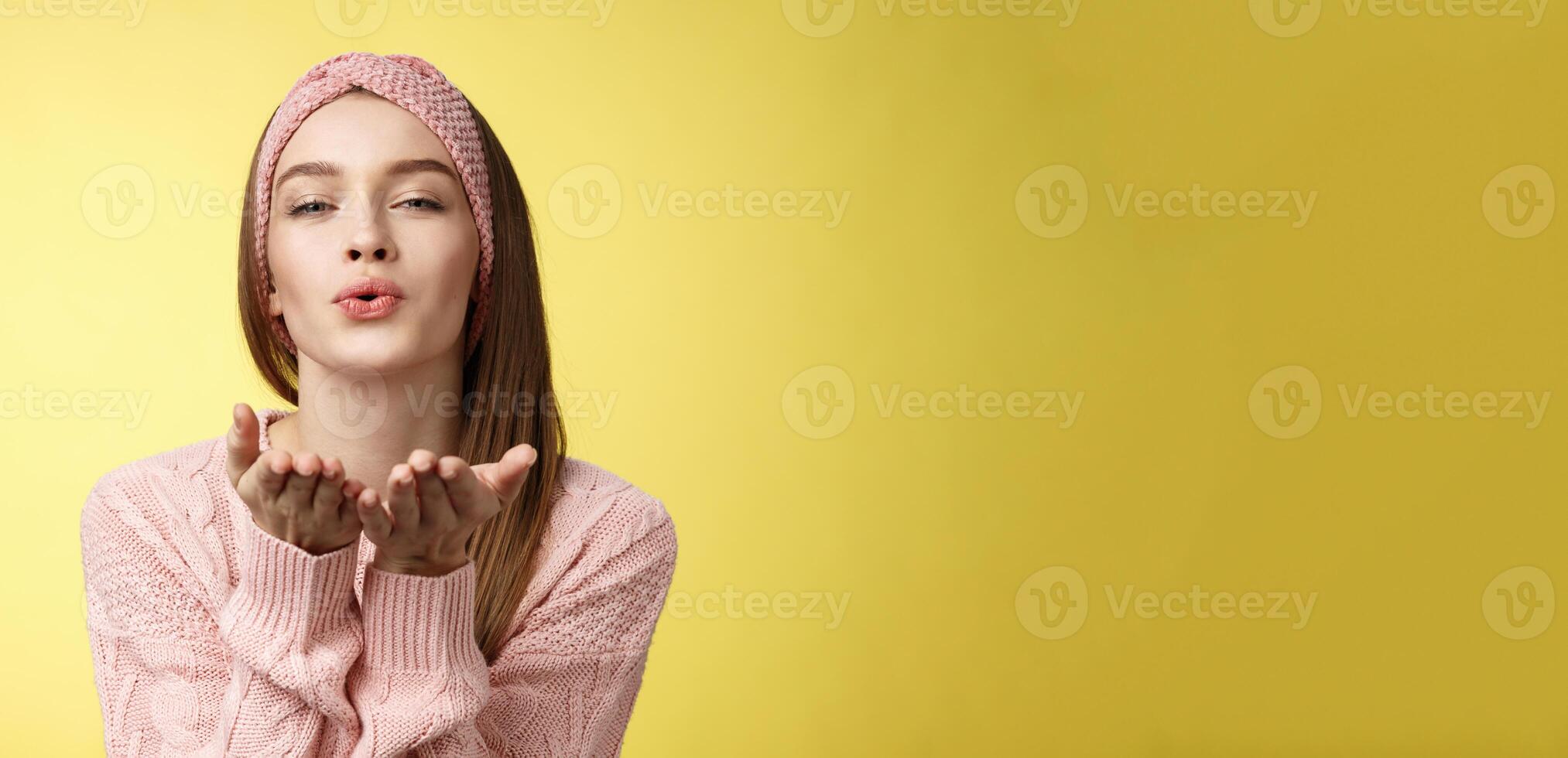 Happy valentines day. Charming romantic and sensual young flirty woman in knitted headband, sweater extending palms near folded lips sending air mwah, blowing kiss tender and gentle photo
