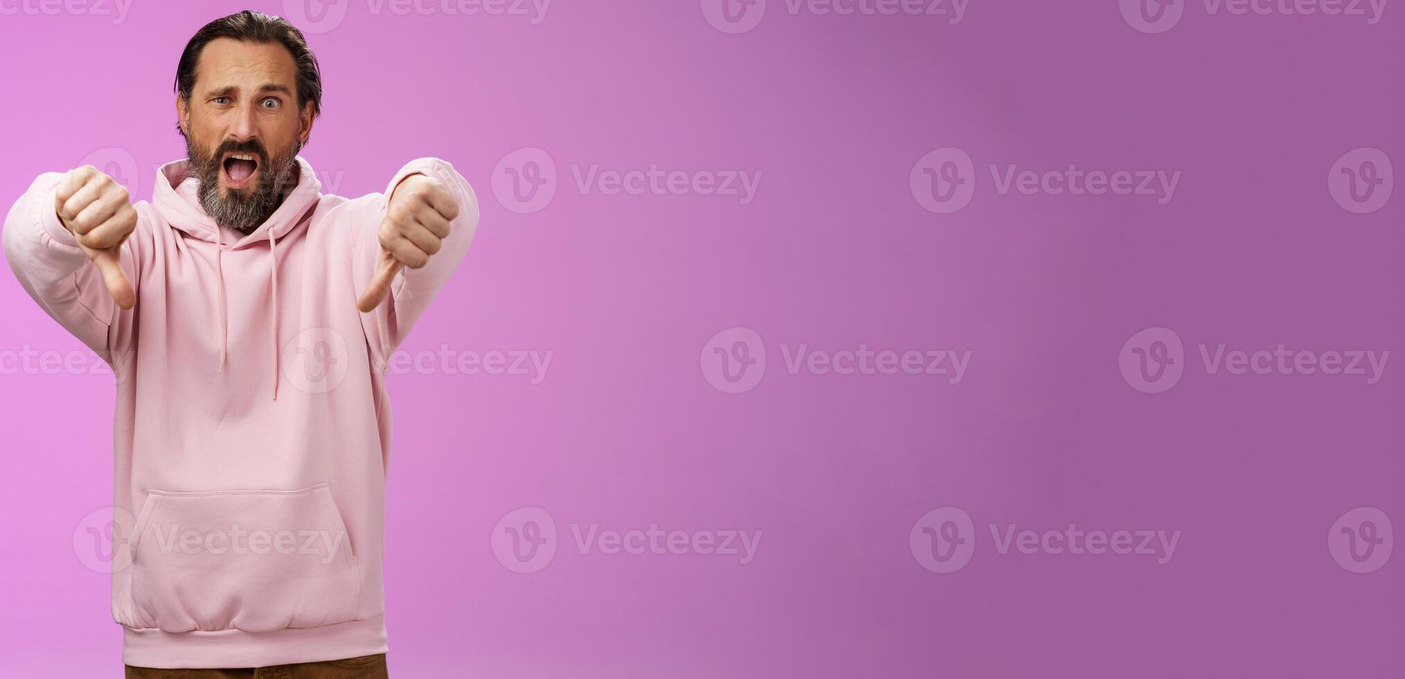 Extremely disappointed furious male customer swearing show thumbs down impulsive gesture yelling displeased pissed express dislike disgust look judgemental bothered, standing purple background photo