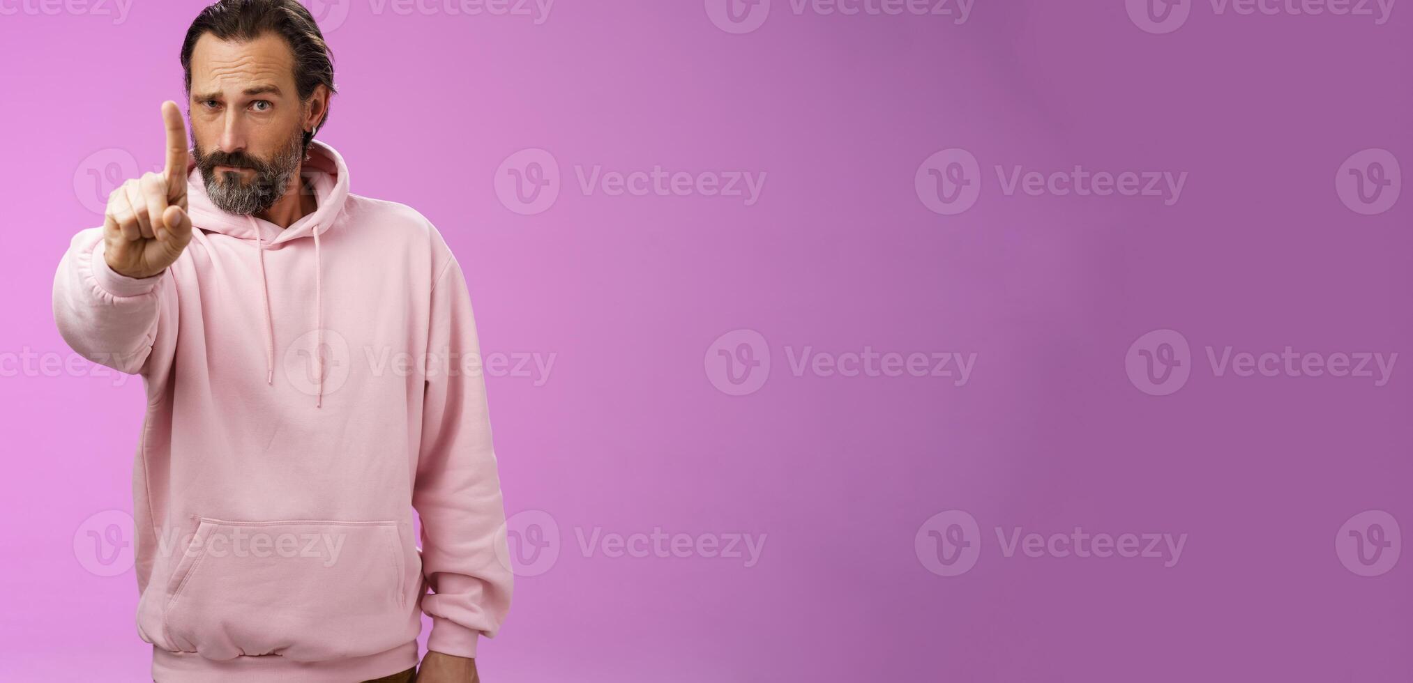 One rule listen. Serious-looking bossy focused determined adult bearded male in pink hoodie extend index finger first number scolding making statement forbid bad behaviour, purple background photo