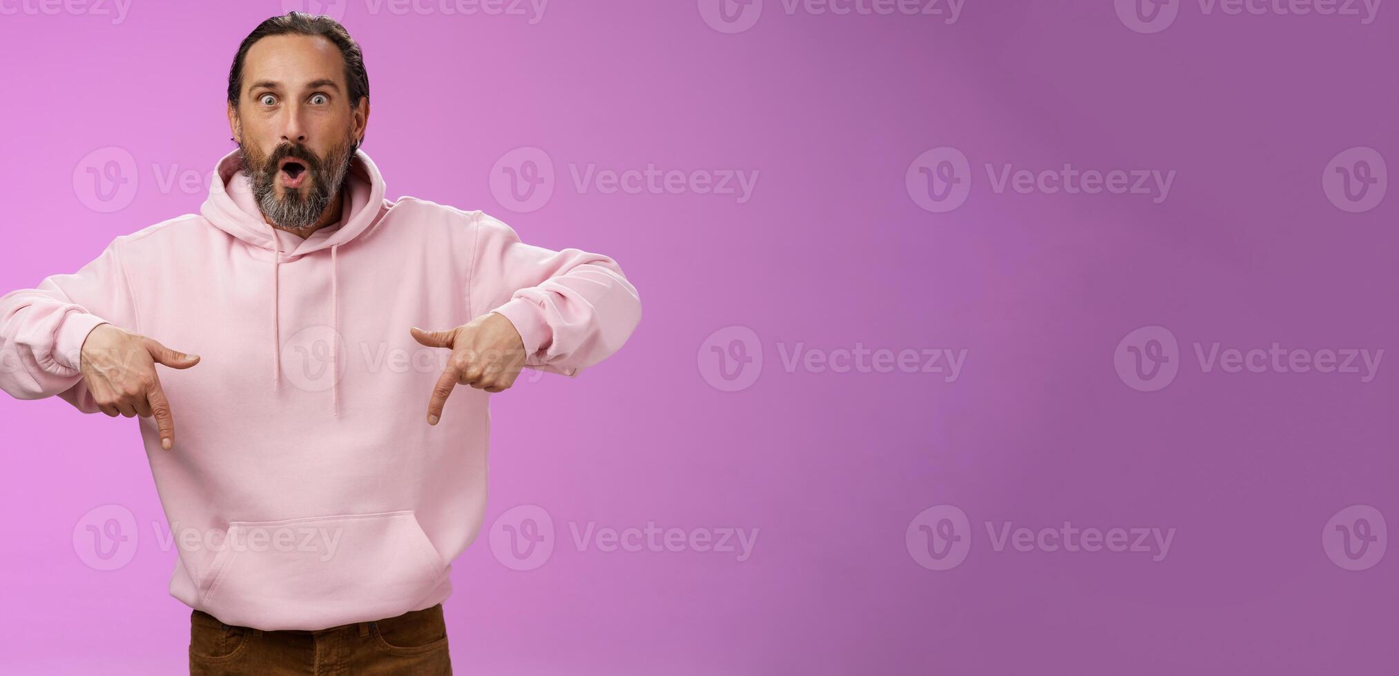 Impressed fascinated speechless dad bearded grey hair say wow widen eyes surprised folding lips amused curiously pointing down index fingers see super amazing advertisement, posing purple background photo