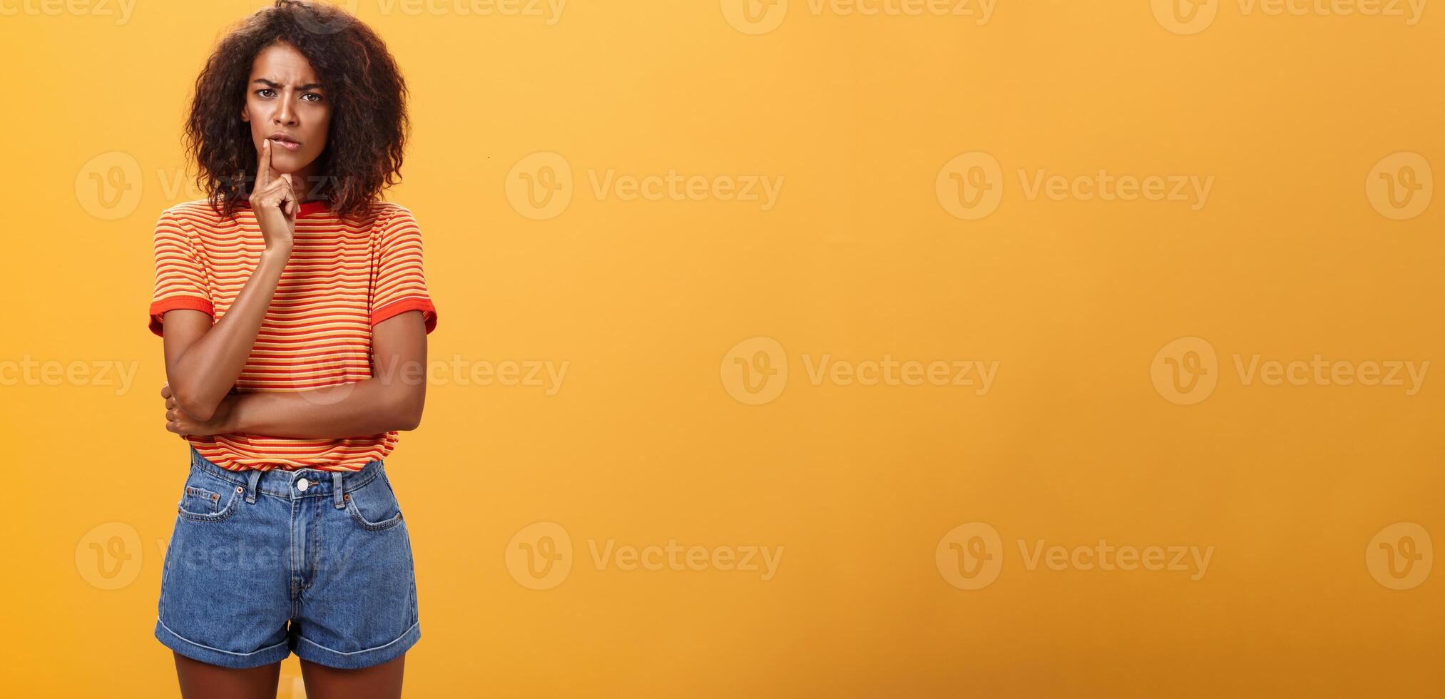Woman looking concerned picking new furniture in store. Thoughtful focused and troubled smart african american businesswoman in casual outfit frowning biting lip touching mouth while thinking photo