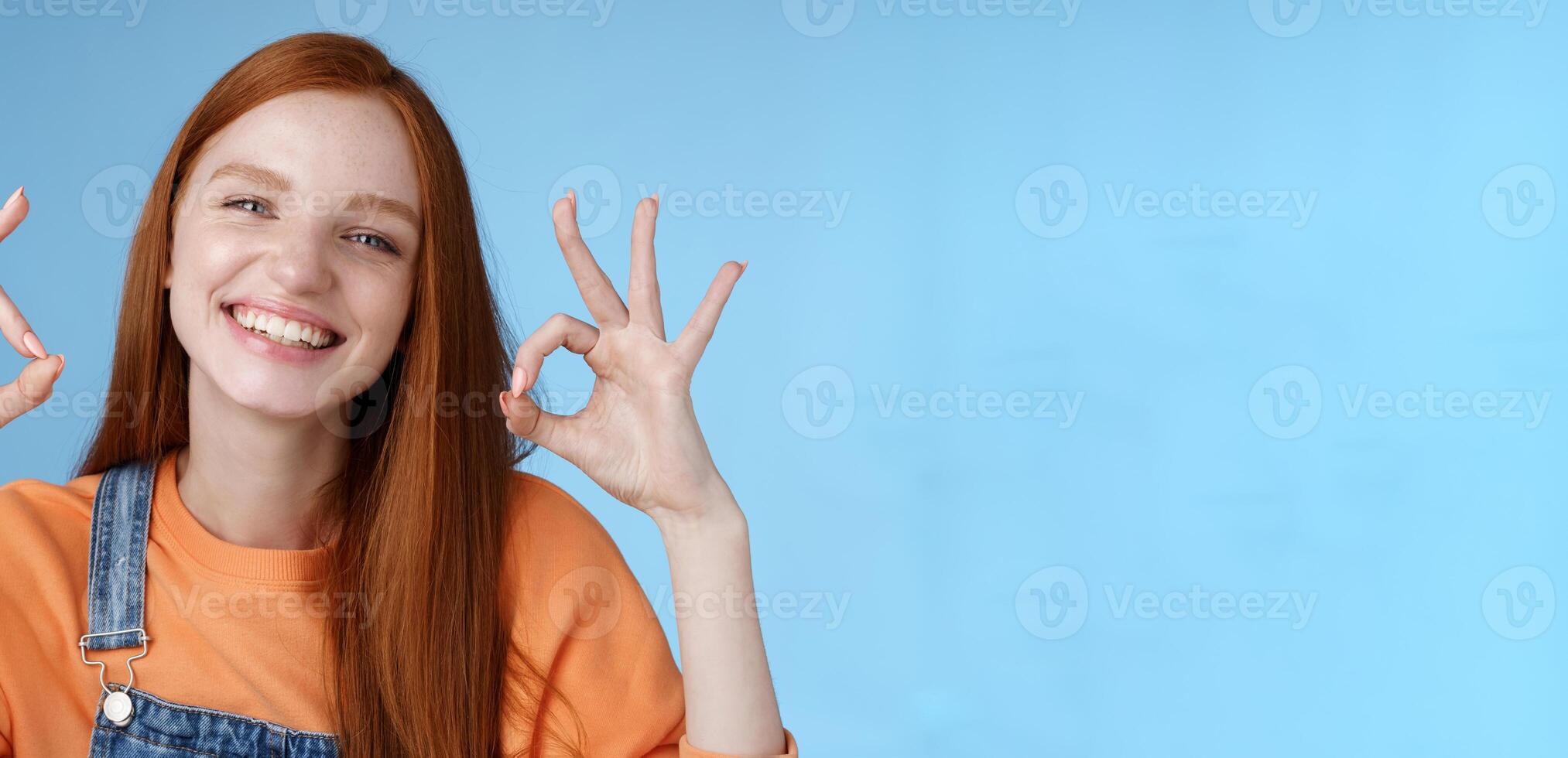 Wellbeing, happiness, perfection concept. Attractive friendly smiling joyful redhead female student show excellent okay ok gestures grinning approval agree awesome concept, satisfied blue background photo