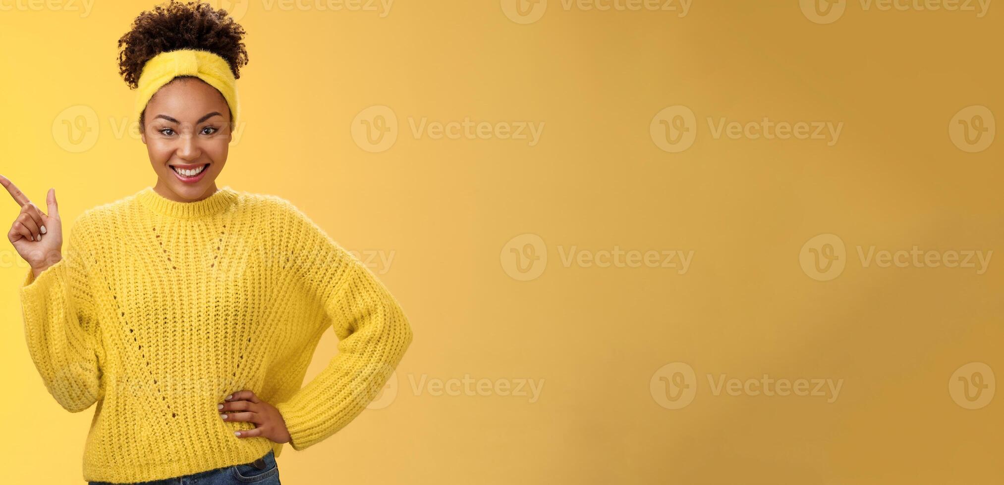 Charming sassy stylish african-american girl in sweater pointing upper left corner standing confident cheeky energized smile yellow background promoting merch showing best choice look camera amused photo