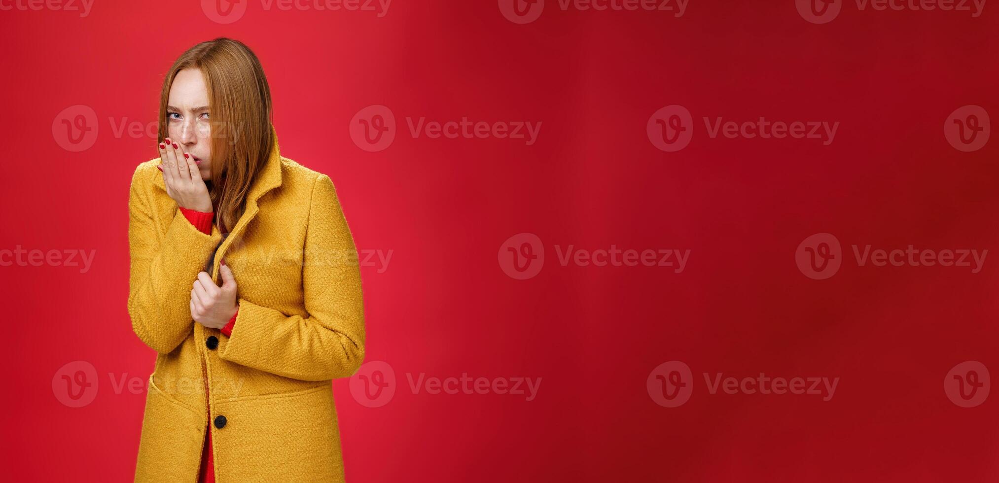 Girl getting cold, coughing and buttoning yelling light coat as freezing on chilly, windy weather looking displeased and ill at camera, feeling unwell catching flu over red background photo