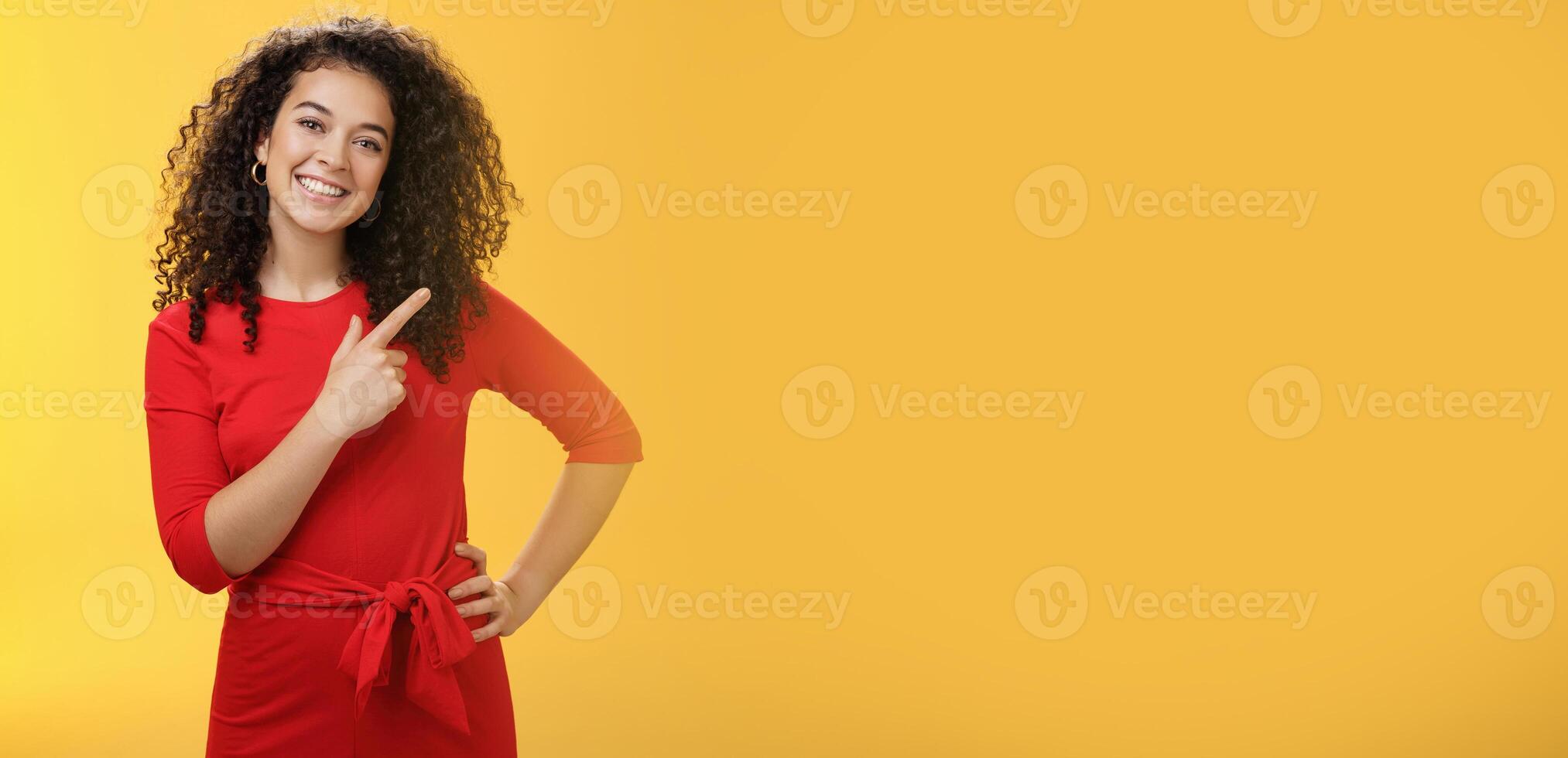 Girl suggesting try out new product. Friendly and pleasant happy young european brunette with curly hair tilting head cute, smiling broadly, pointing at upper right corner to direct at advertisement photo