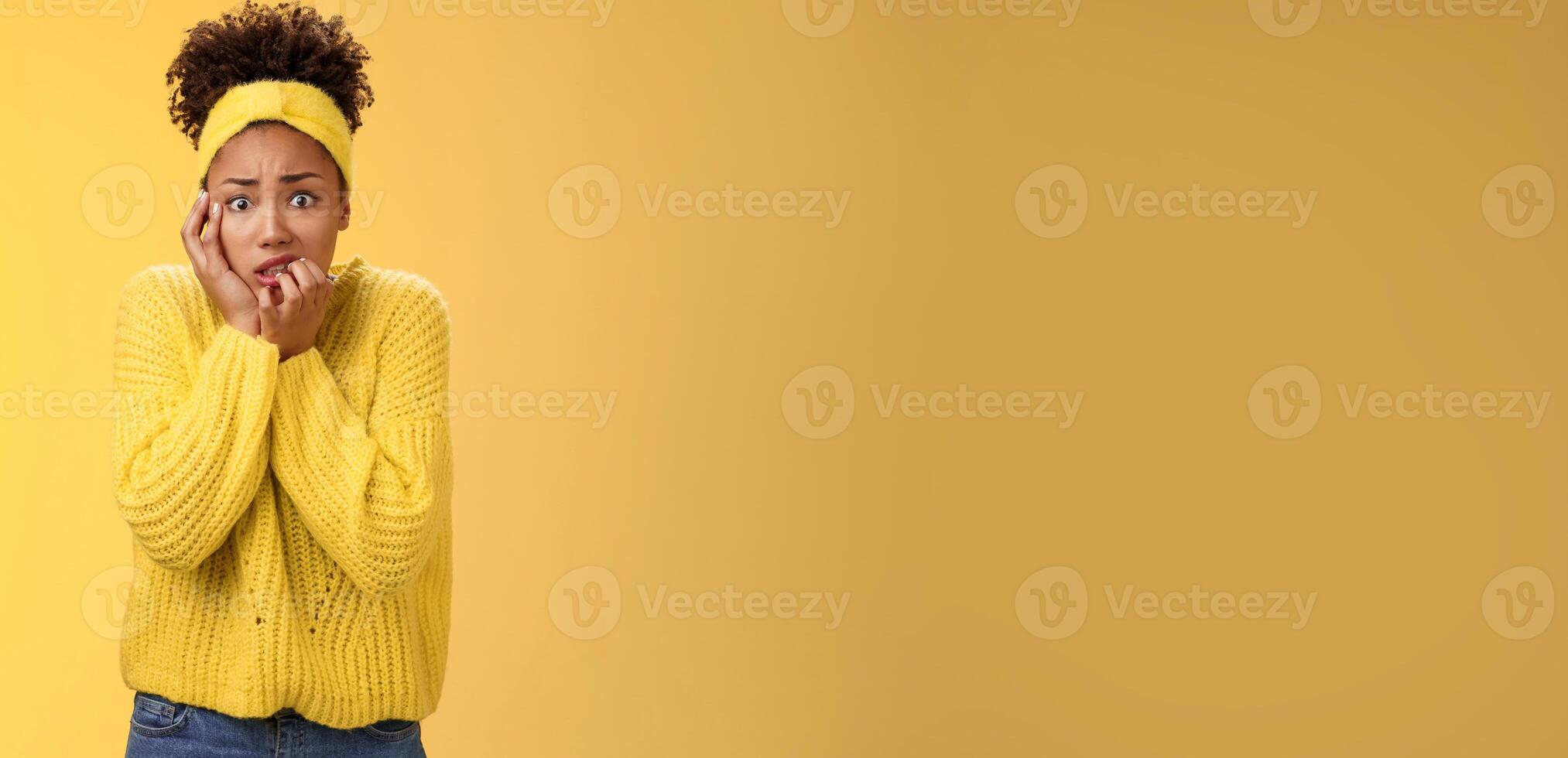 Afraid concerned nervous young african american female employee worried anxious be fired clench teeth stooping touch face insecure bit fingers standing scared terrified, yellow background photo