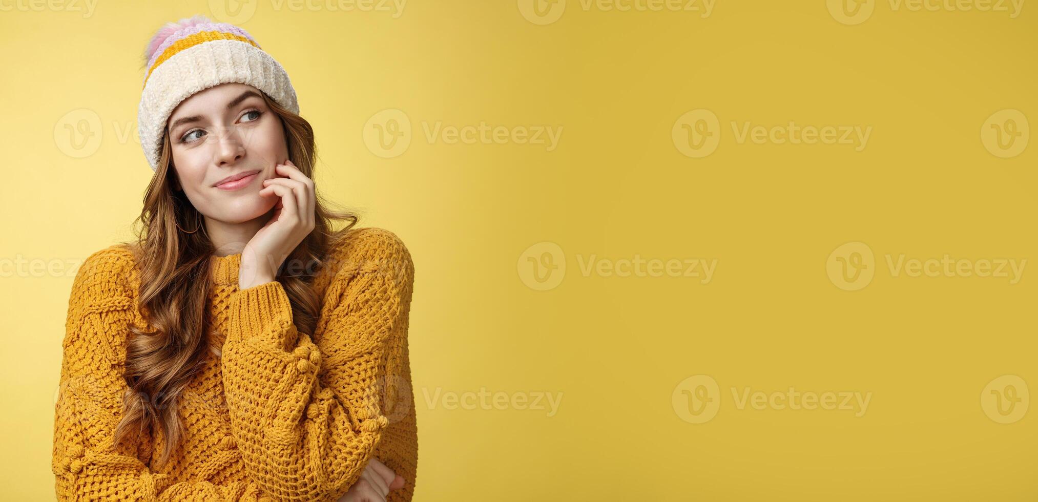 Dreamy creative charming girlfriend wearing warm hat sweater gazing right thoughtful imaging romantic date smiling happily picturing recalling lovely memories, standing delighted yellow background photo